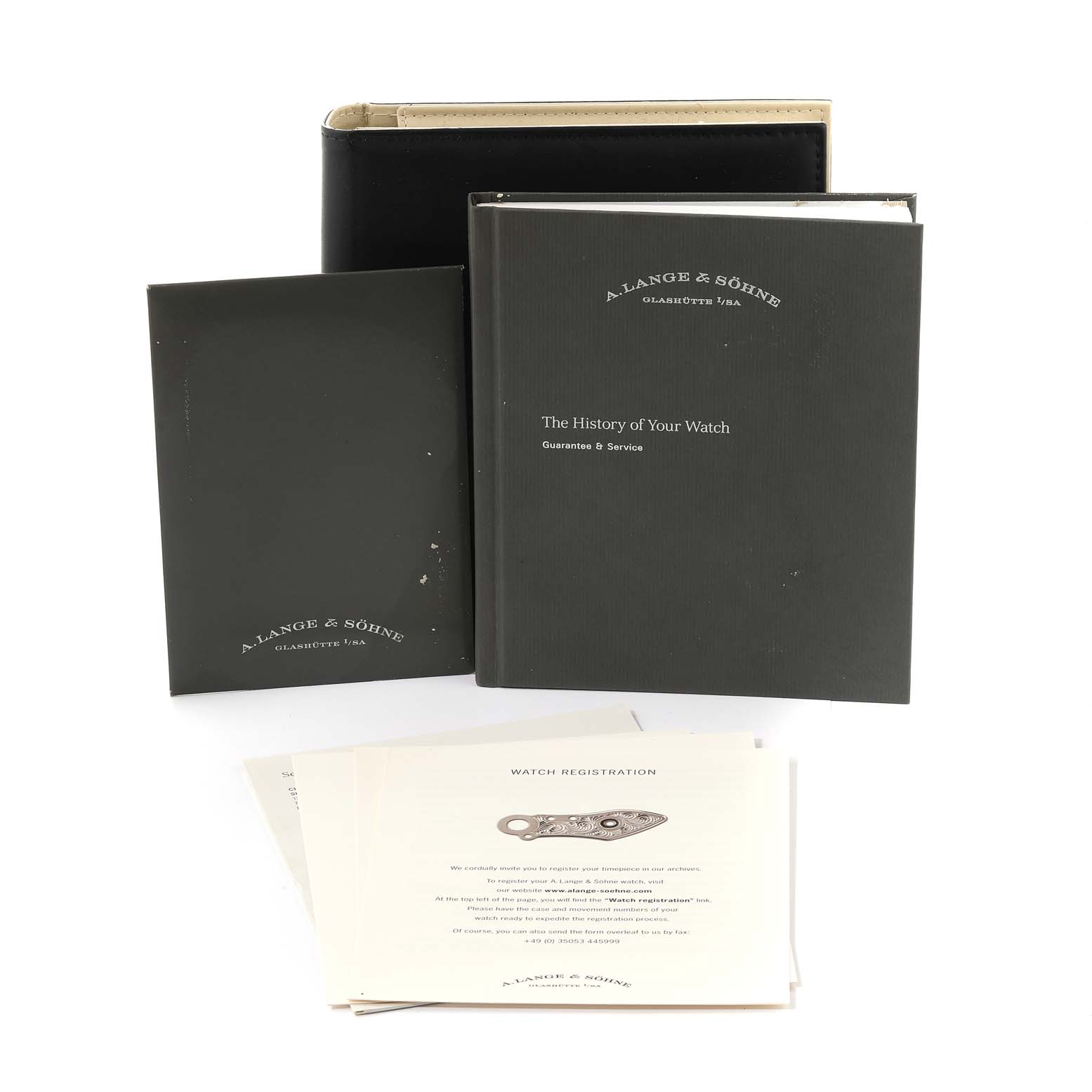 The image shows an A. Lange & Sohne Lange 1 117.028 Men's White Gold Black Dial model with its accompanying documentation and case, including booklets and registration cards.