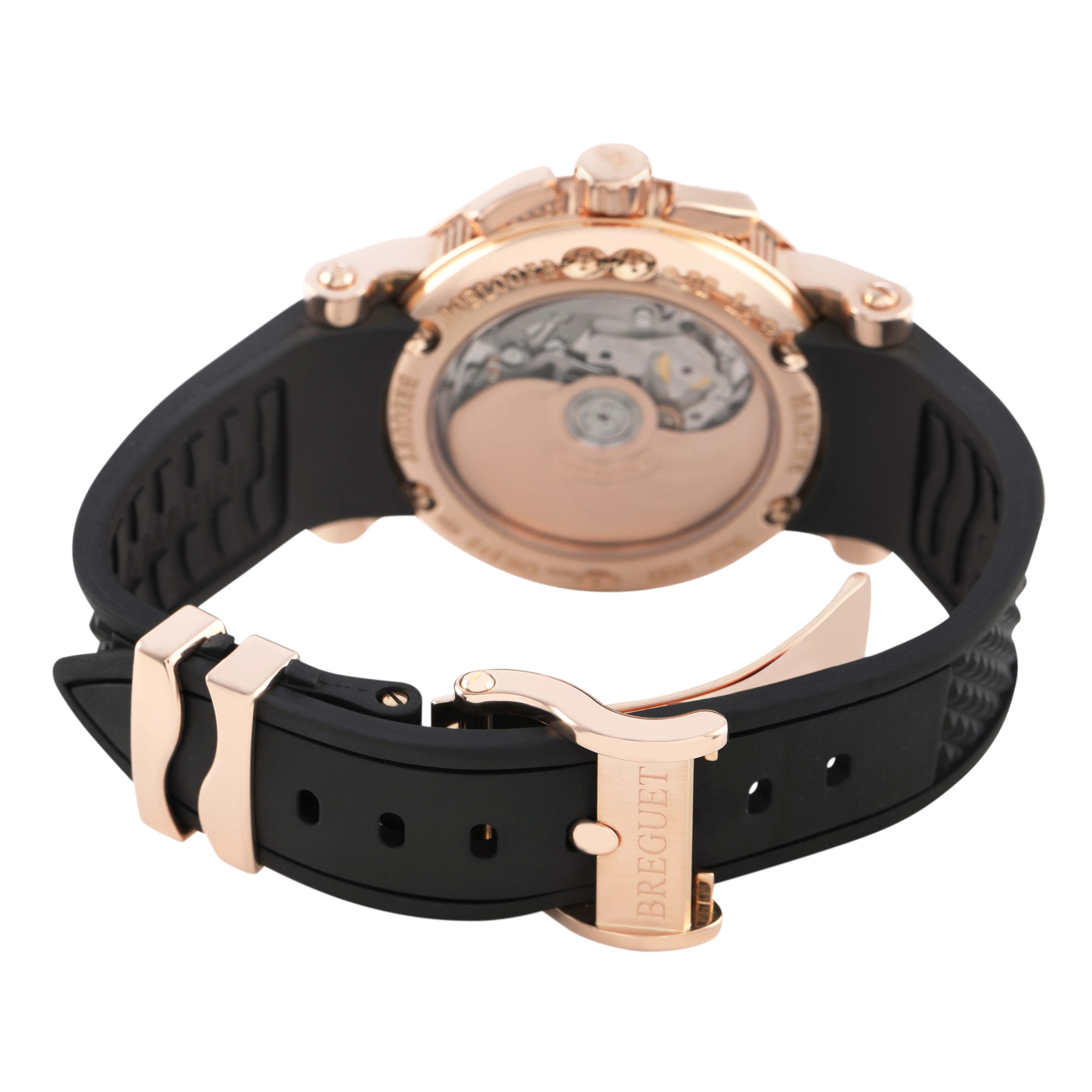 The Breguet Marine 5827BR/Z2/5ZU Men's Yellow Gold Silver Dial watch is shown from the back, displaying its movement and rubber strap with a gold clasp.