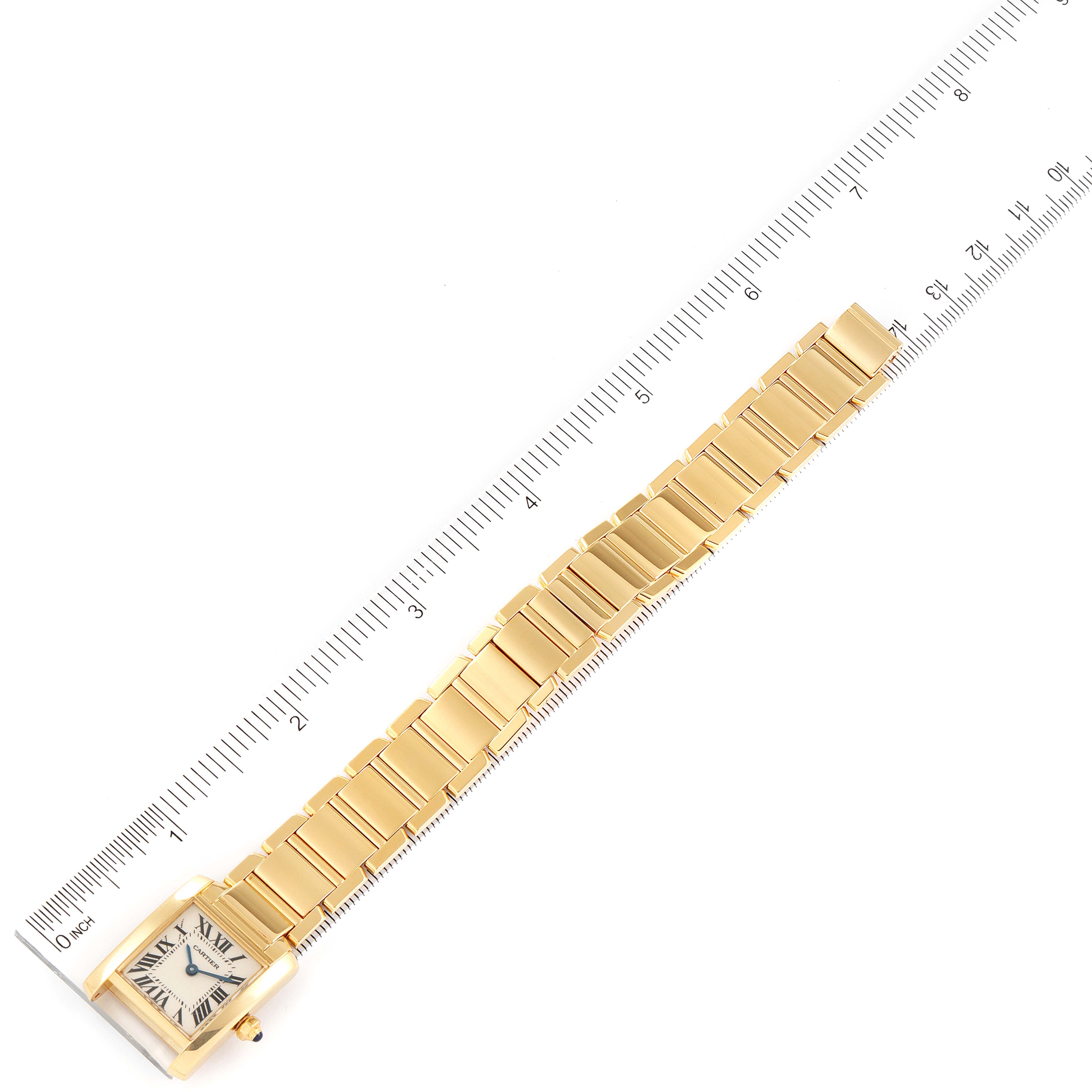 The image shows a top-down view of a Cartier Tank Francaise W50002N2 Women's Yellow Gold Silver Dial W50002N2 Women's Yellow Gold Silver Dial watch, highlighting its gold bracelet and square face next to a ruler.
