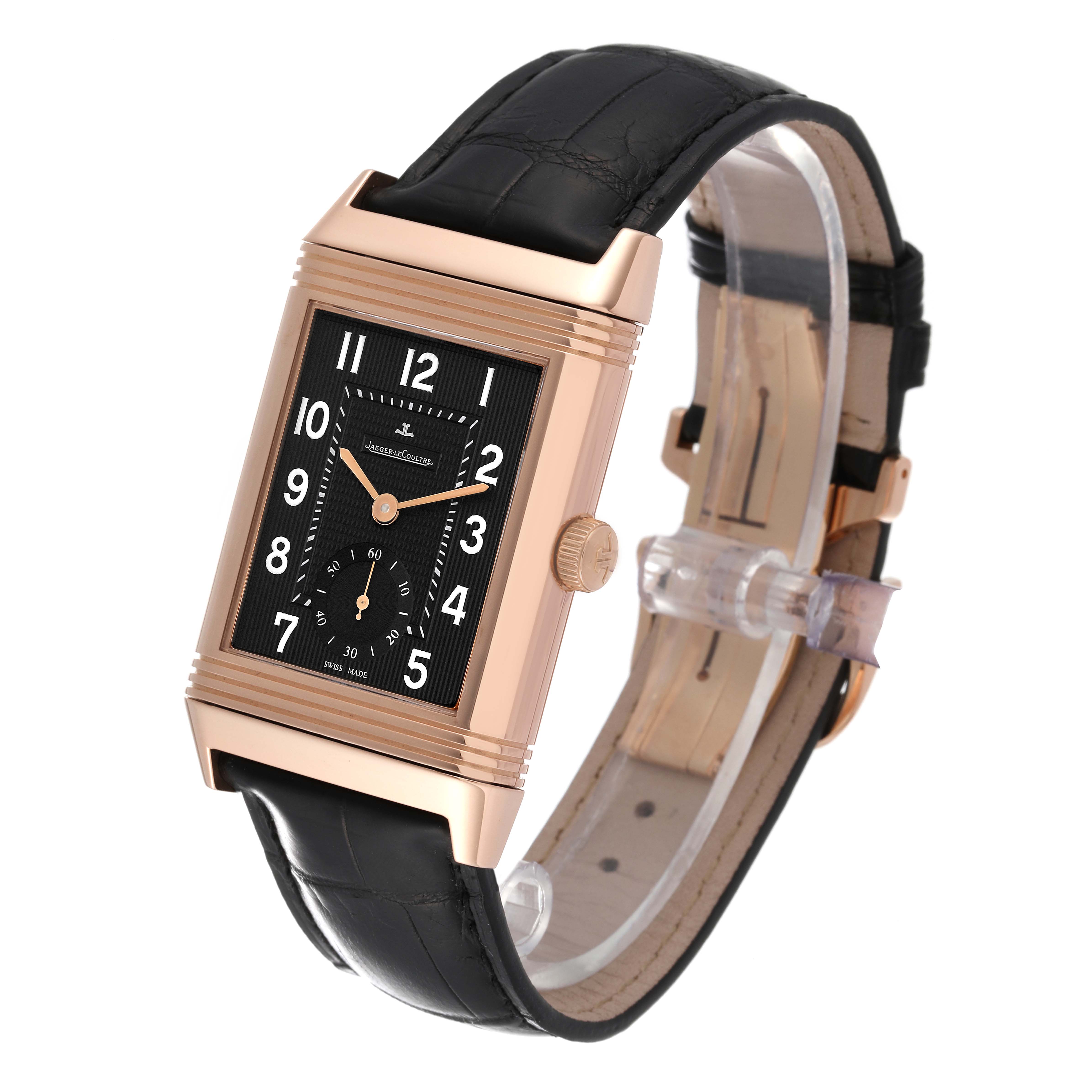 The Jaeger-LeCoultre Reverso watch is shown at a three-quarter angle, highlighting the black dial, gold case, and black leather strap.