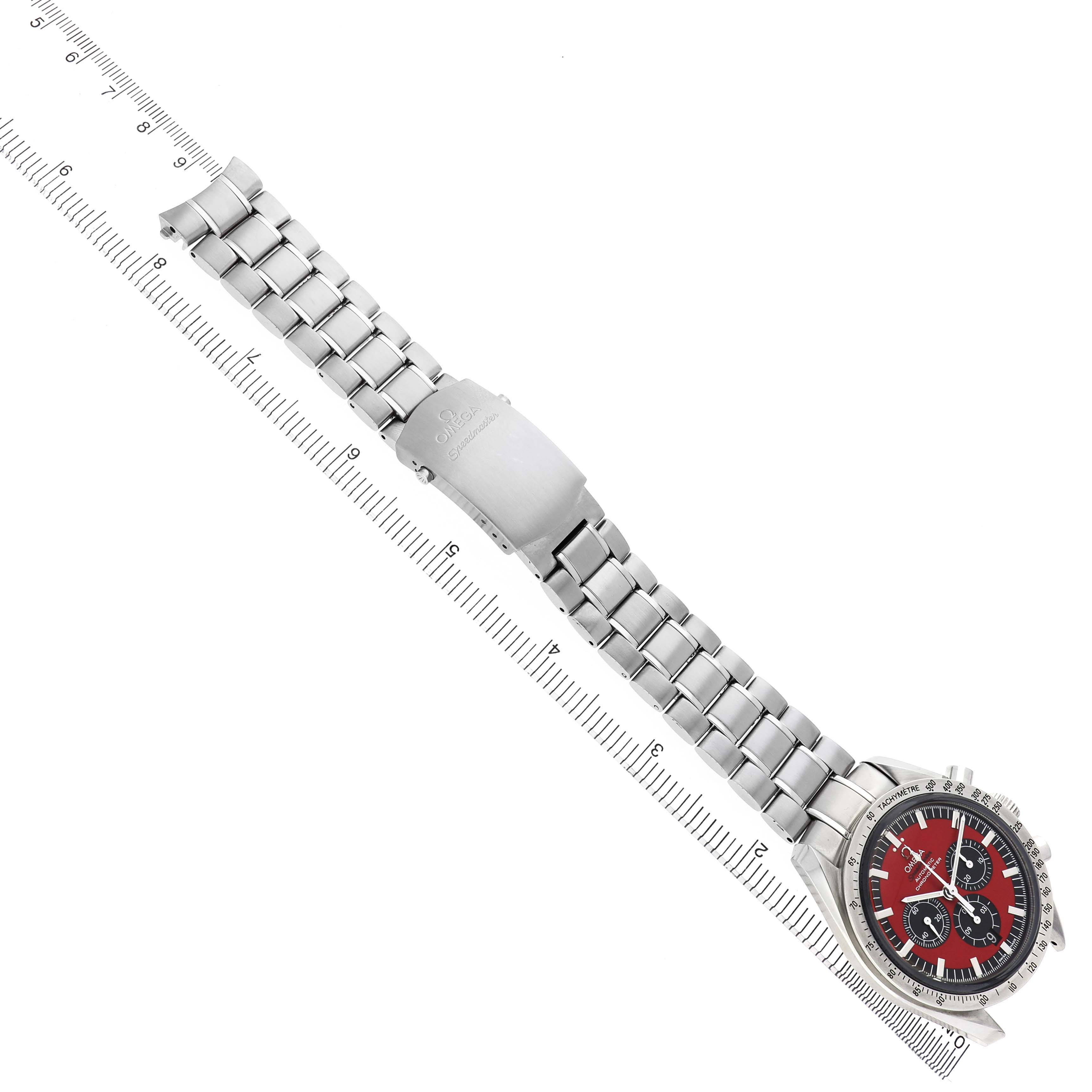The Omega Speedmaster 3506.61.00 Men's Stainless Steel Red Dial watch is shown at an overhead angle, with the bracelet extended and a ruler for scale.