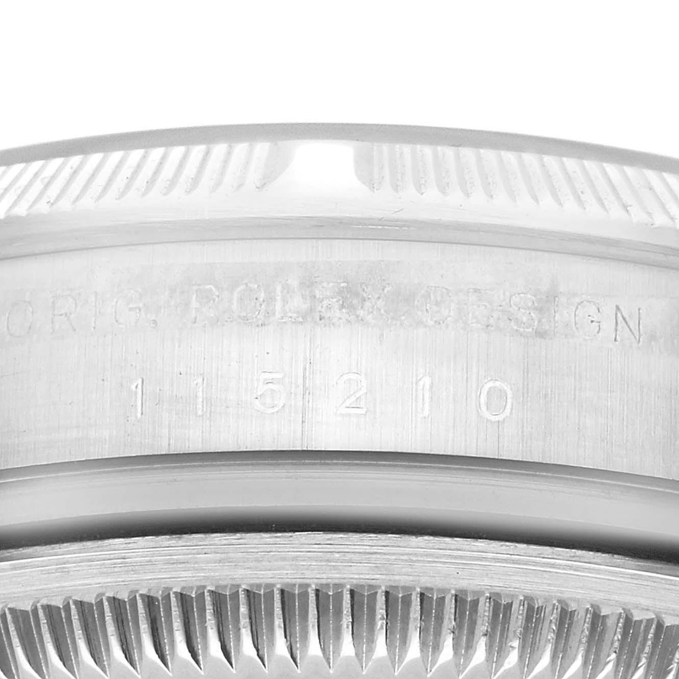 The image shows a detailed close-up of the side of a Rolex Date 115210 Men's Stainless Steel Blue Dial 115210 Men's Stainless Steel Blue Dial model watch, highlighting the engraved serial number and design.