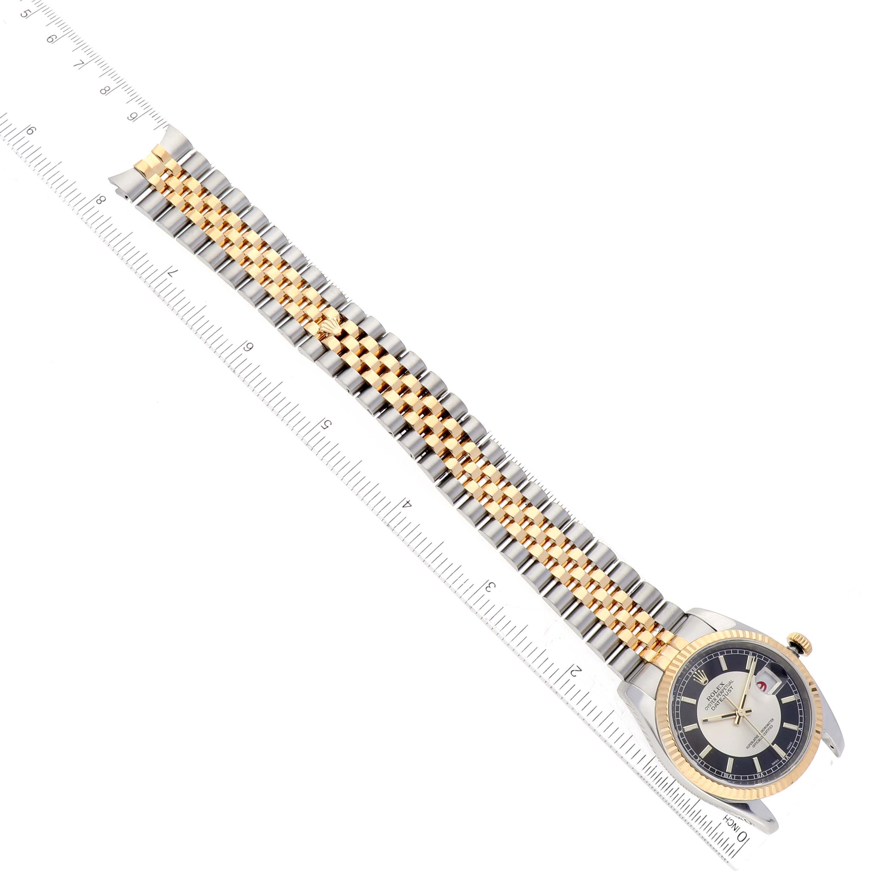 This image shows a Rolex Datejust 116233 Men's Stainless Steel Black Dial 116233 Men's Stainless Steel Black Dial watch with a two-tone gold and silver bracelet, positioned diagonally and placed alongside a ruler.