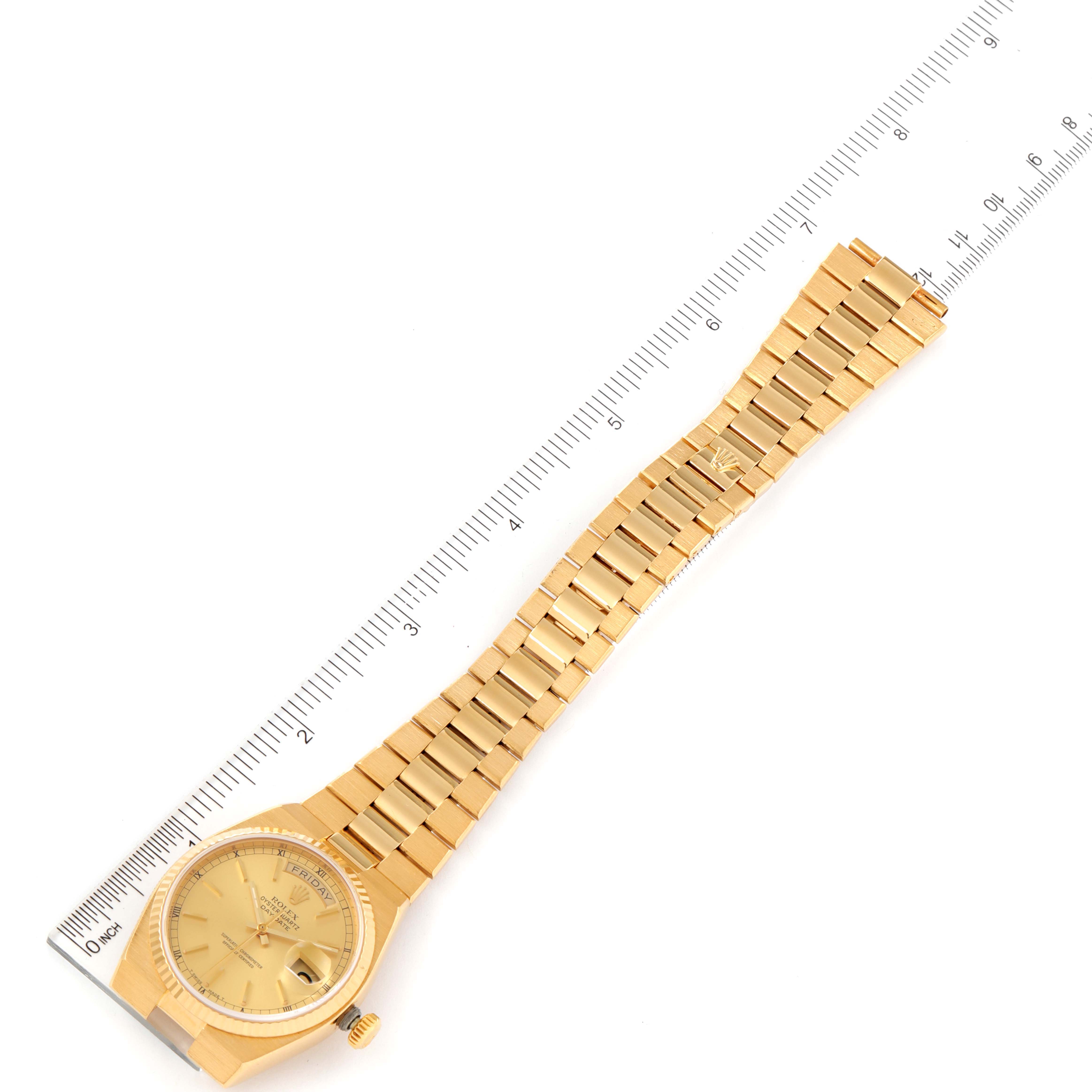 The Rolex Oysterquartz 19018 Men
s Yellow Gold Champagne Dial 19018 Men
s Yellow Gold Champagne Dial watch is shown from a top-down view, displaying the dial, bracelet, and part of a measuring ruler.