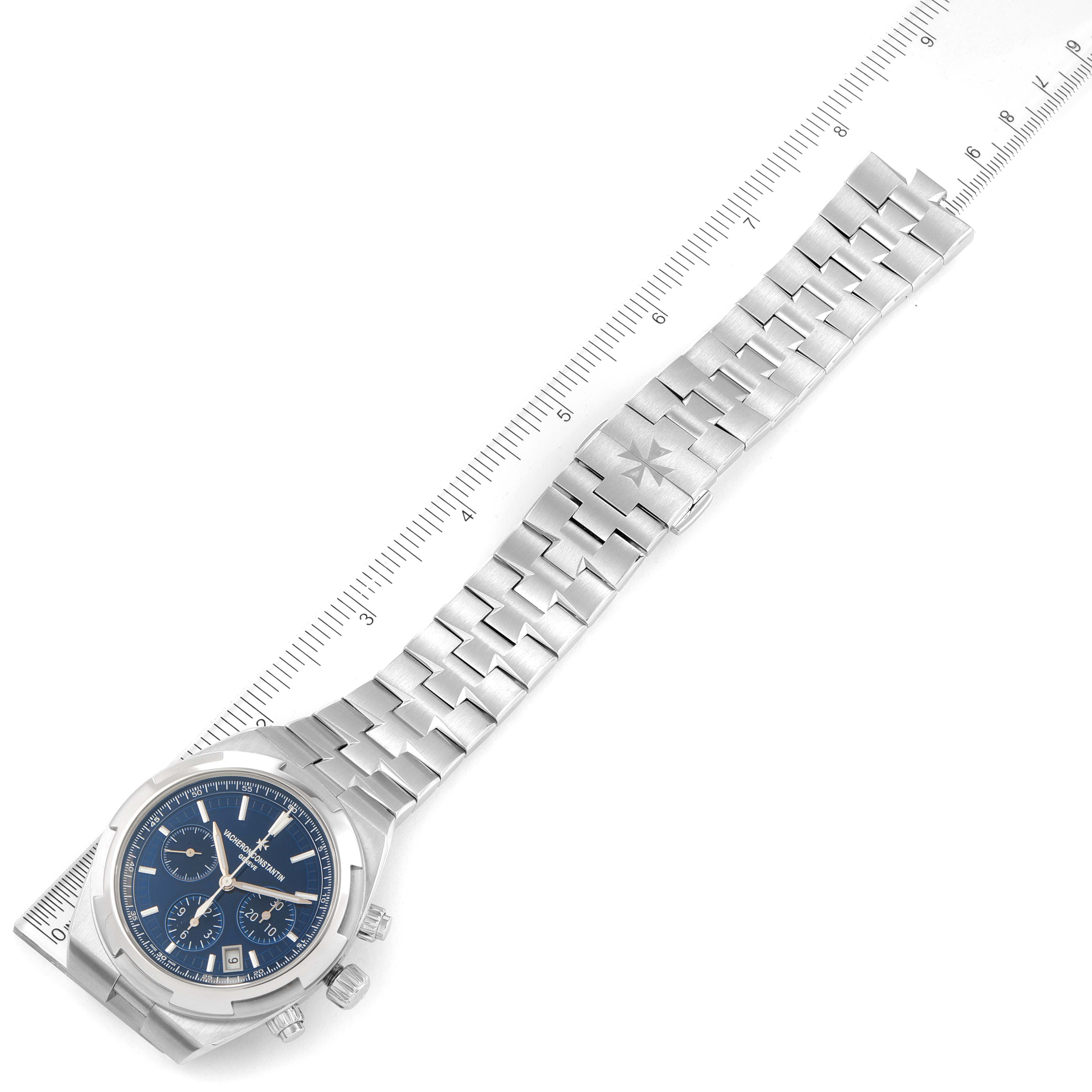 The image shows a Vacheron Constantin Overseas 5500V/110A-B148 Men's Stainless Steel Blue Dial 5500V/110A-B148 Men's Stainless Steel Blue Dial model watch laid flat with its bracelet extended alongside a ruler.