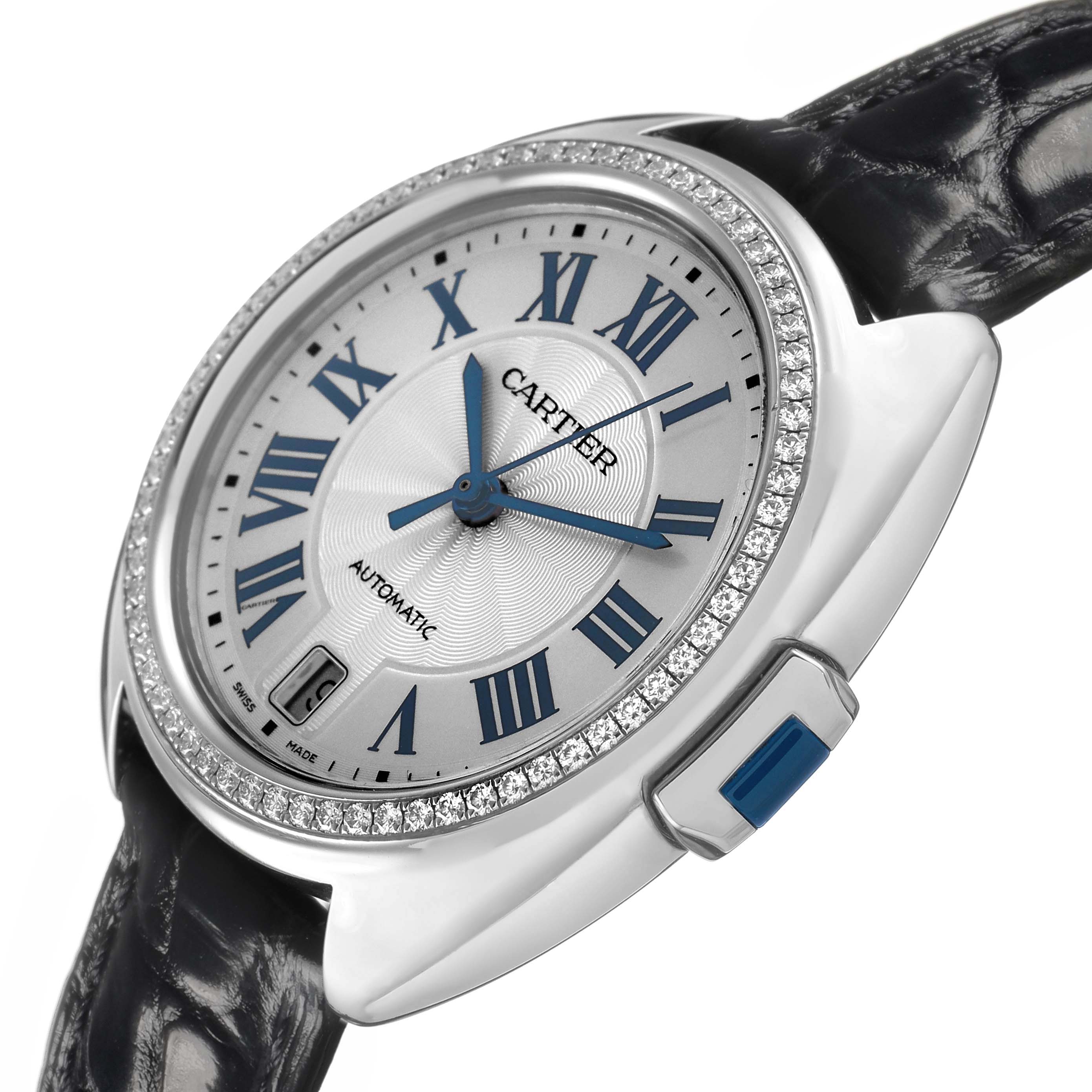 The Cartier Clé watch is shown at an angle highlighting the dial, bezel with diamonds, and blue Roman numerals.