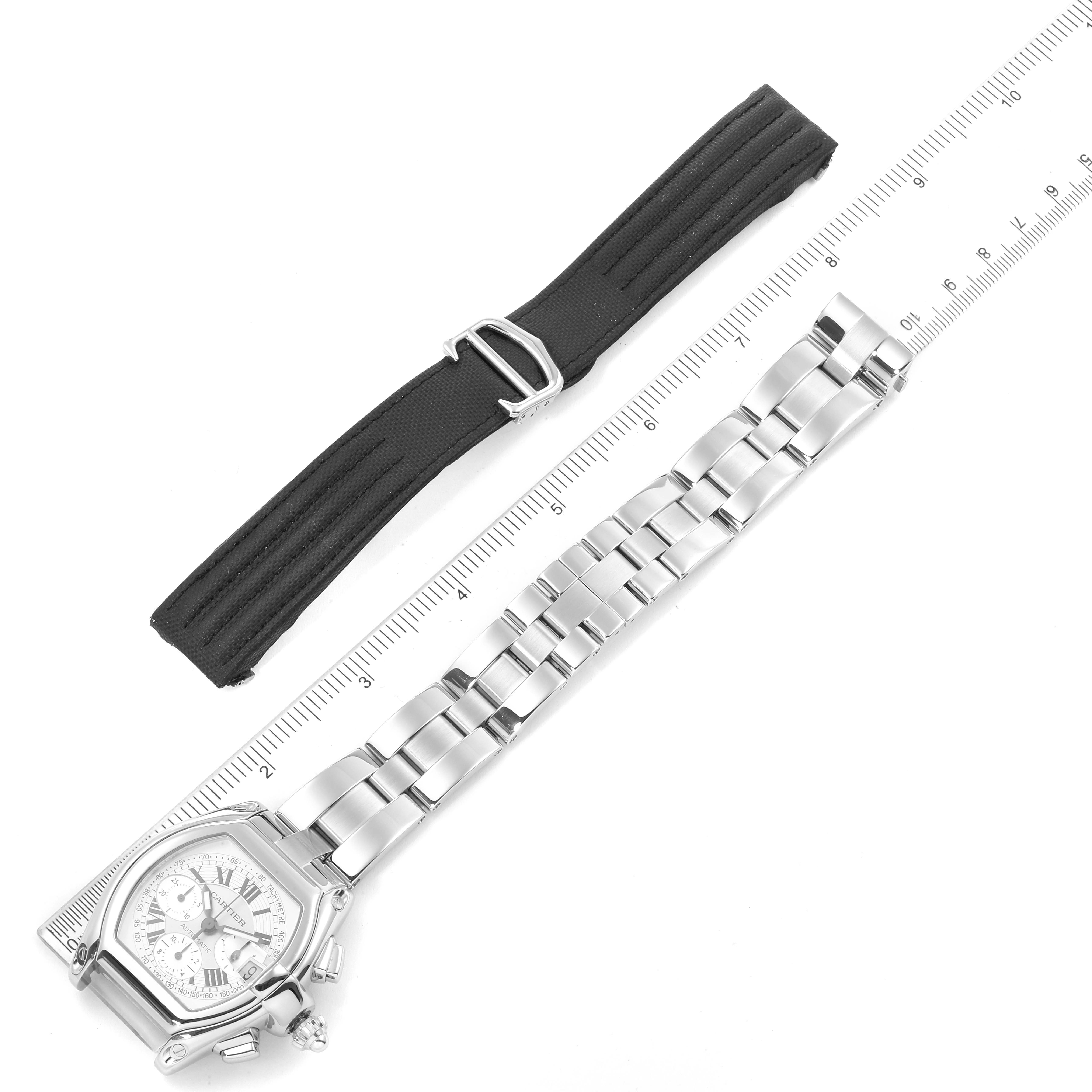 The image shows the Cartier Roadster W62006X6 Men
s Stainless Steel Silver Dial W62006X6 Men
s Stainless Steel Silver Dial watch and its metal bracelet along with a black rubber strap, viewed from the top next to a ruler.