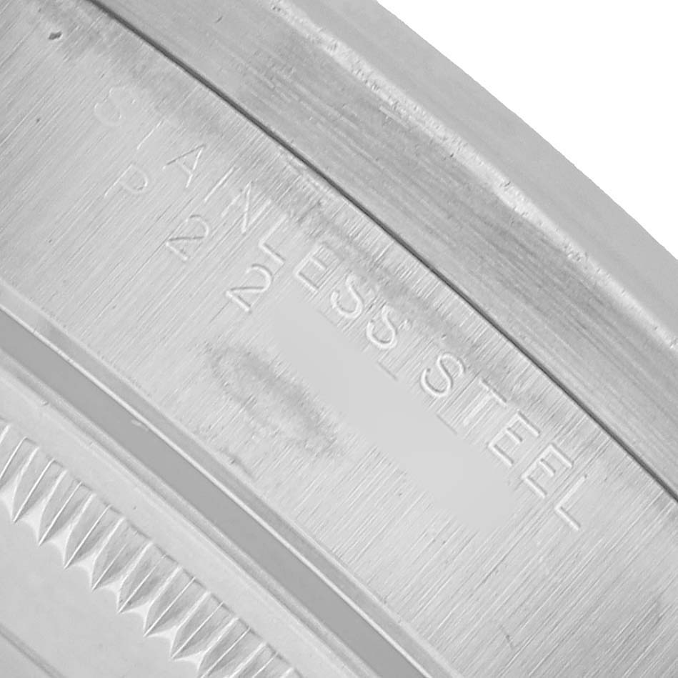 The image shows a close-up of a Rolex Date 15210 Men's Stainless Steel Blue Dial model's stainless steel case, focusing on the engraved text and bezel edge.