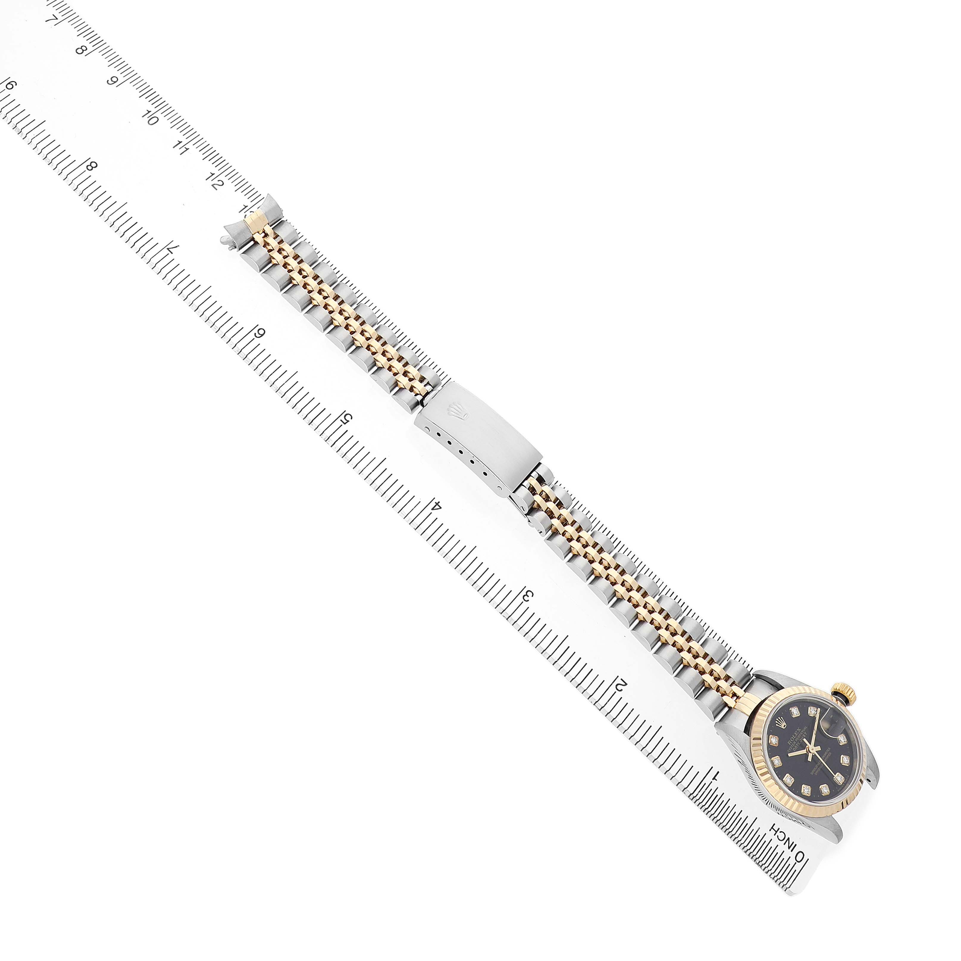 The Rolex Datejust 79173 Women's Steel and Gold (two tone) Black Dial watch is shown diagonally, displaying its dial, case, bracelet, and clasp alongside a ruler for measurement.