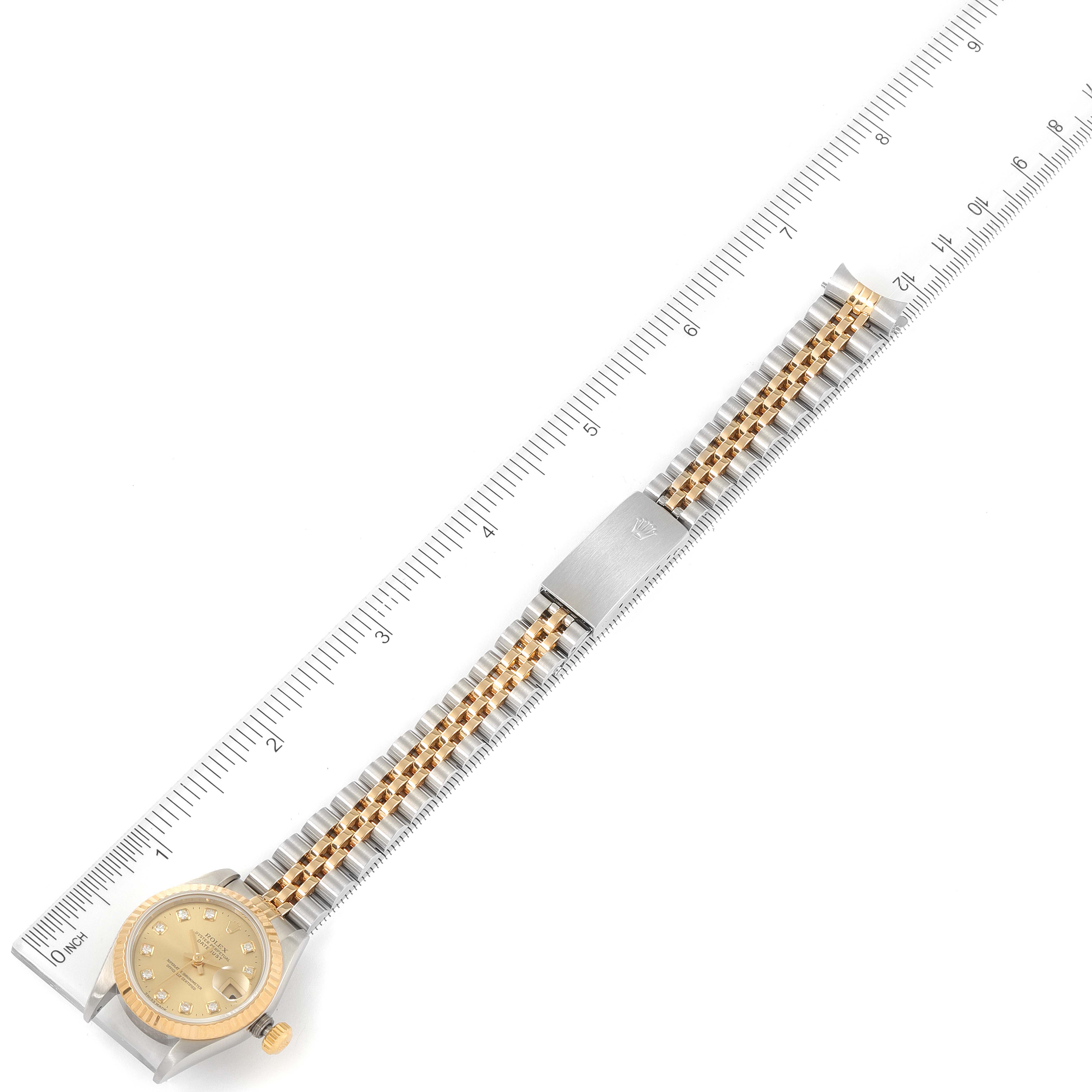 The image shows a top view of the Rolex Datejust 69173 Women
s Steel and Gold (two tone) Champagne Dial 69173 Women
s Steel and Gold (two tone) Champagne Dial watch, featuring the face, bracelet, and clasp next to a ruler.
