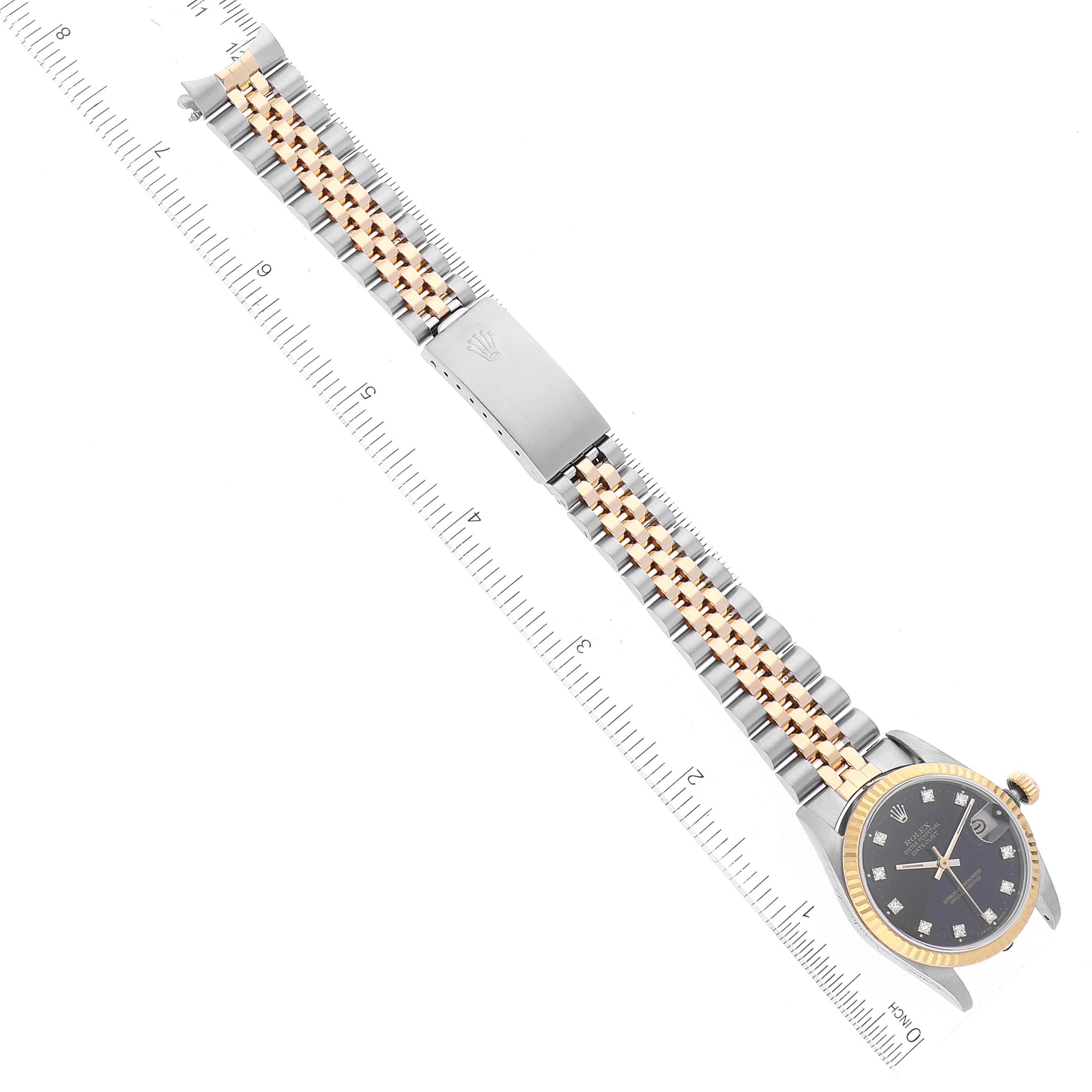 The image shows an overhead view of a Mid-Size Rolex watch with a two-tone bracelet and closed clasp, alongside a ruler for scale.