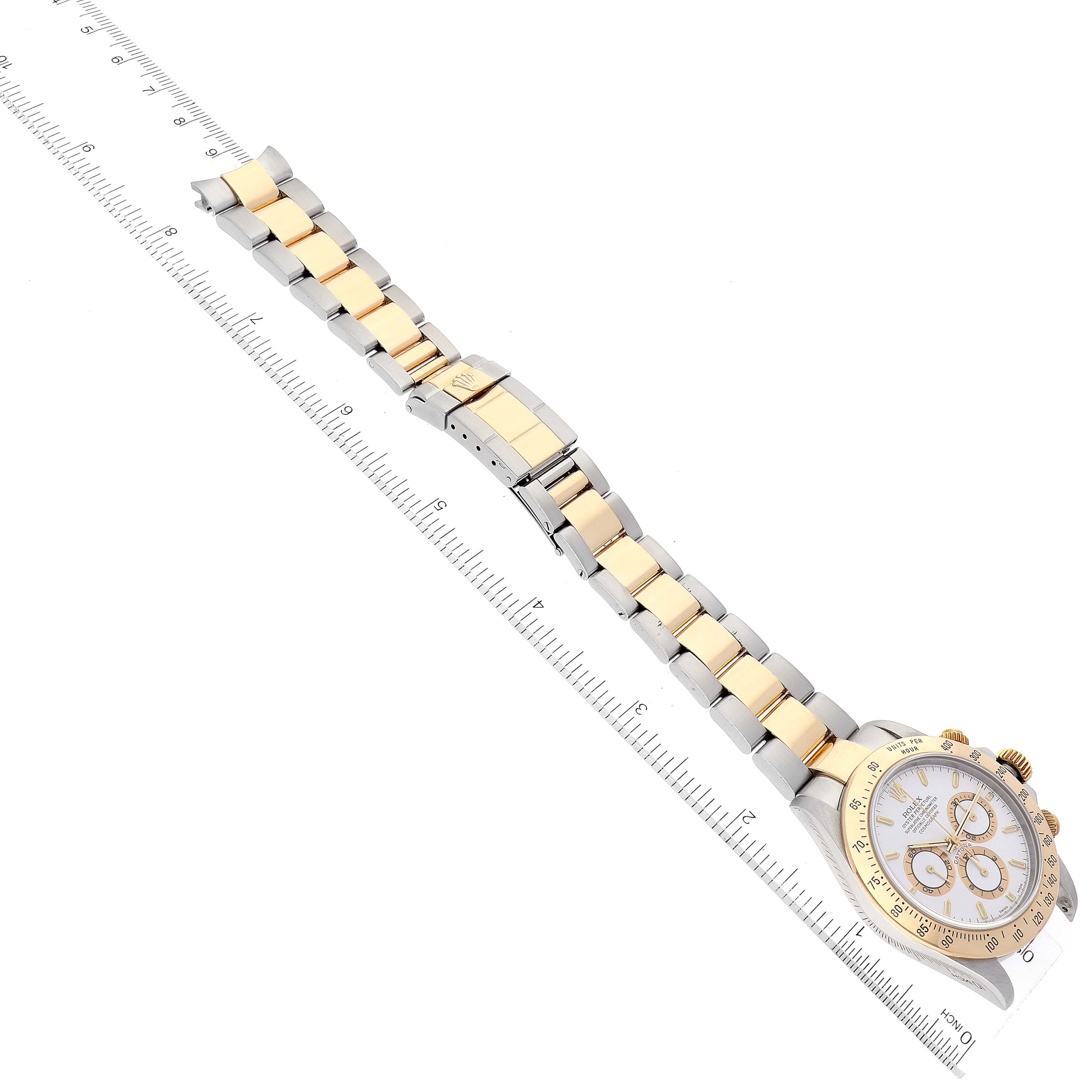 This image features a Rolex Daytona 16523 Men
s Steel and Gold (two tone) White Dial 16523 Men
s Steel and Gold (two tone) White Dial watch laid flat with the full band extended and aligned along a measuring ruler.