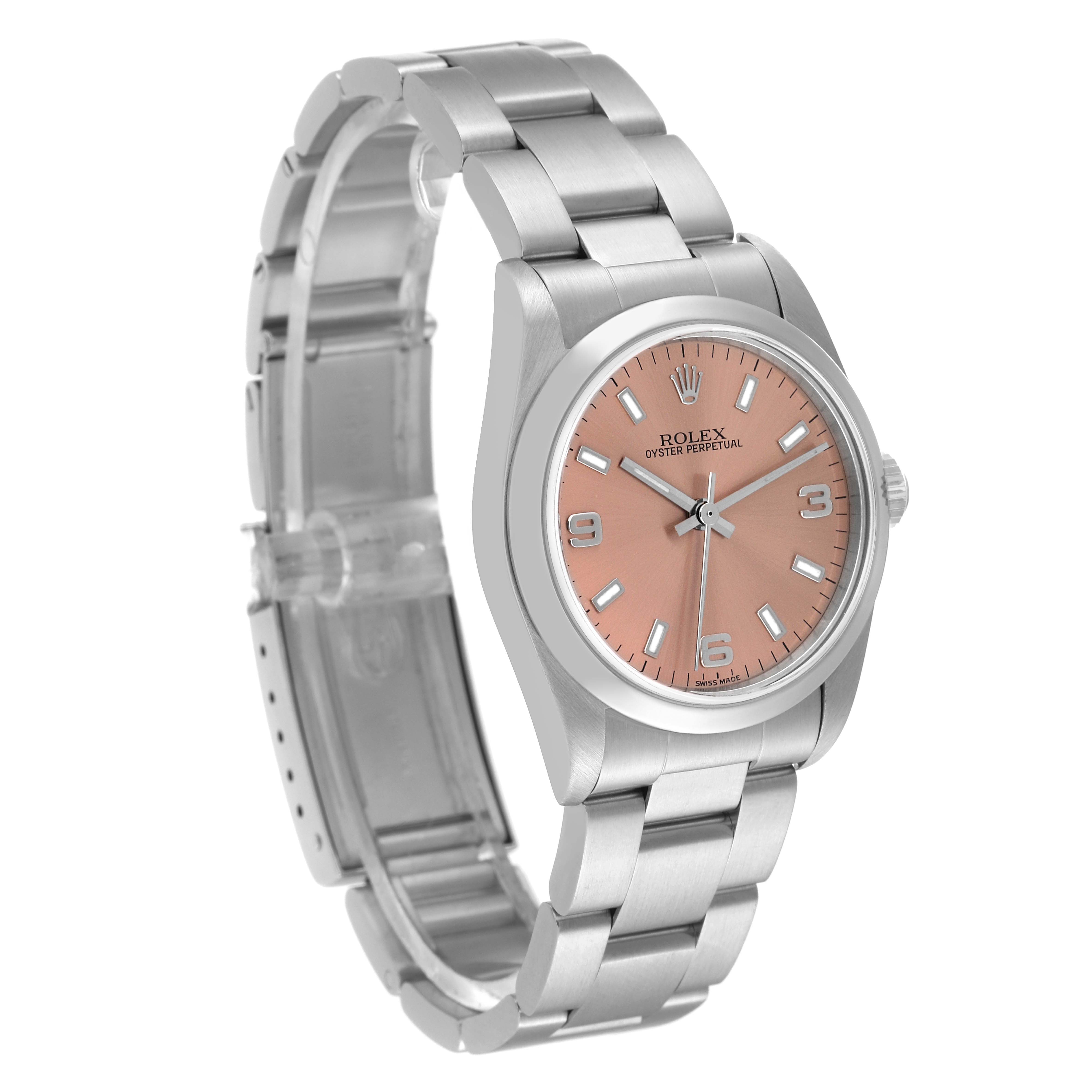 The image shows a Rolex Mid-Size 77080 Women
s Stainless Steel Pink Dial 77080 Women
s Stainless Steel Pink Dial watch from an angled view, highlighting its silver band, salmon dial, and three-hand mechanism.