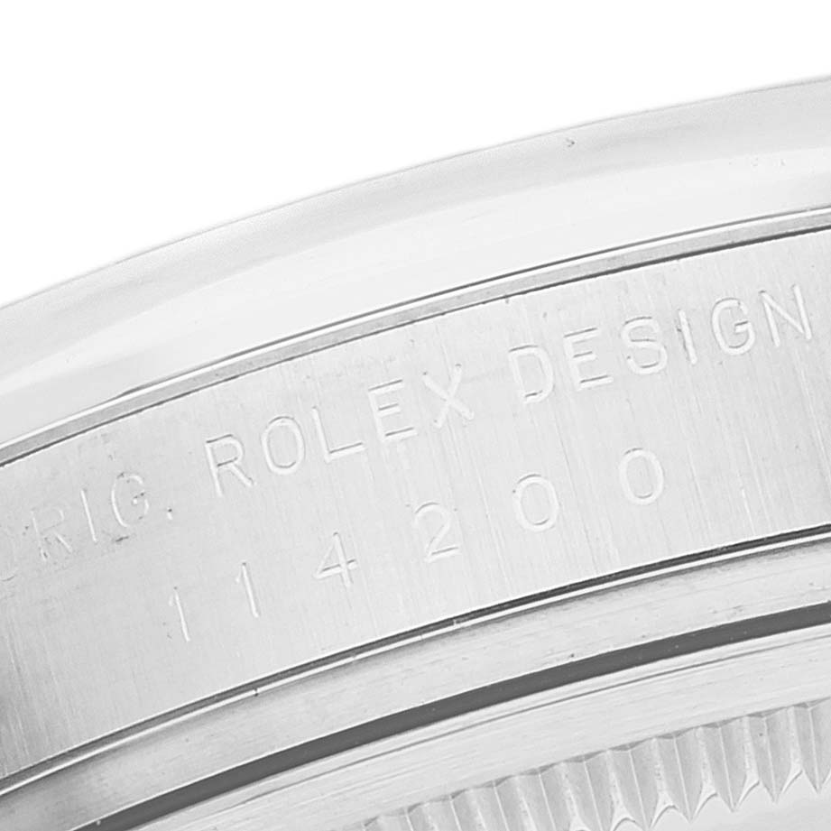 This image shows a close-up, angled view of the engraved case back edge of a Rolex Oyster Perpetual 114200 Men's Stainless Steel White Dial 114200 Men's Stainless Steel White Dial watch.