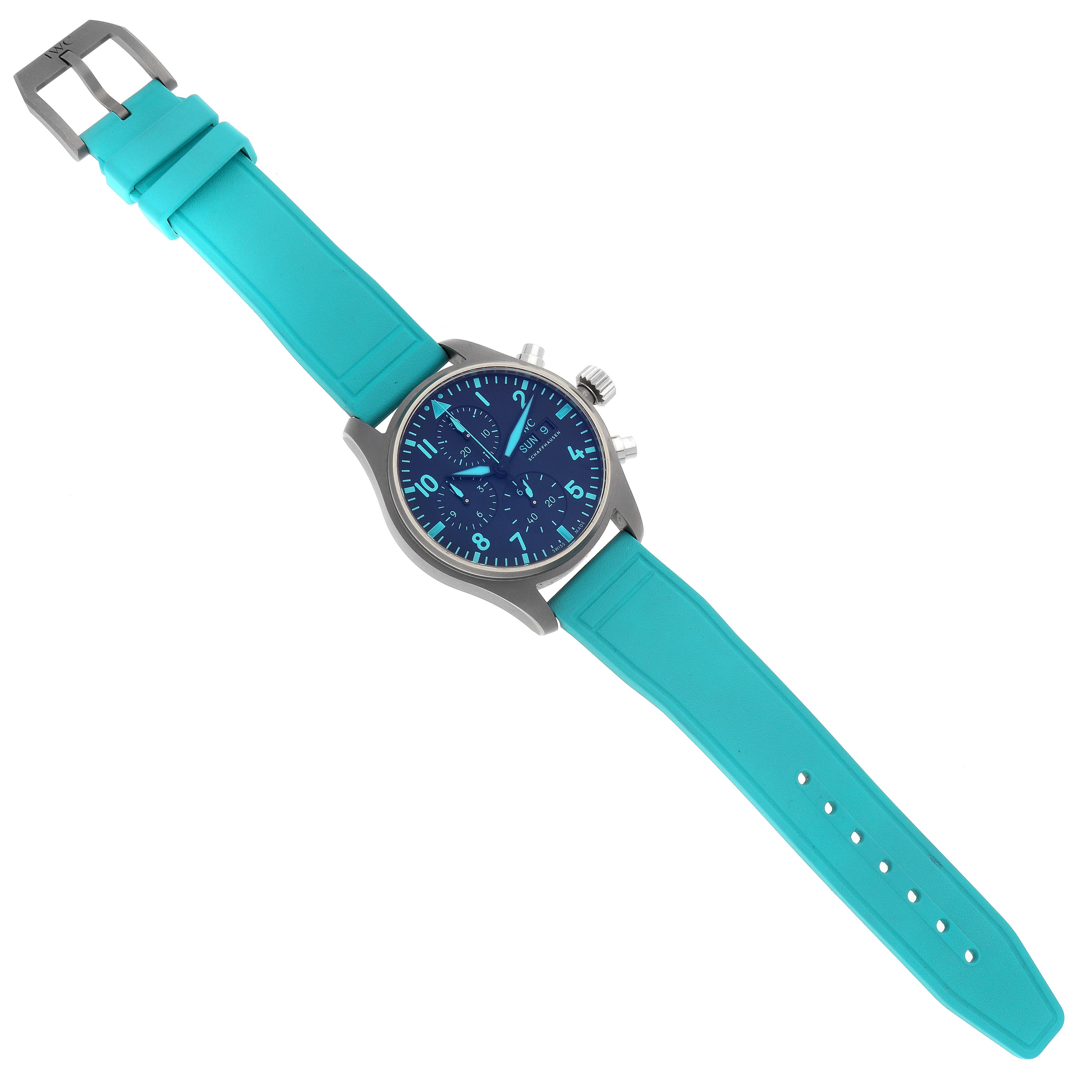 The IWC Pilot IW388108 Men's Titanium Black Dial IW388108 Men's Titanium Black Dial watch is shown at a top-down angle, displaying its teal strap and blue dial with visible pushers and crown.