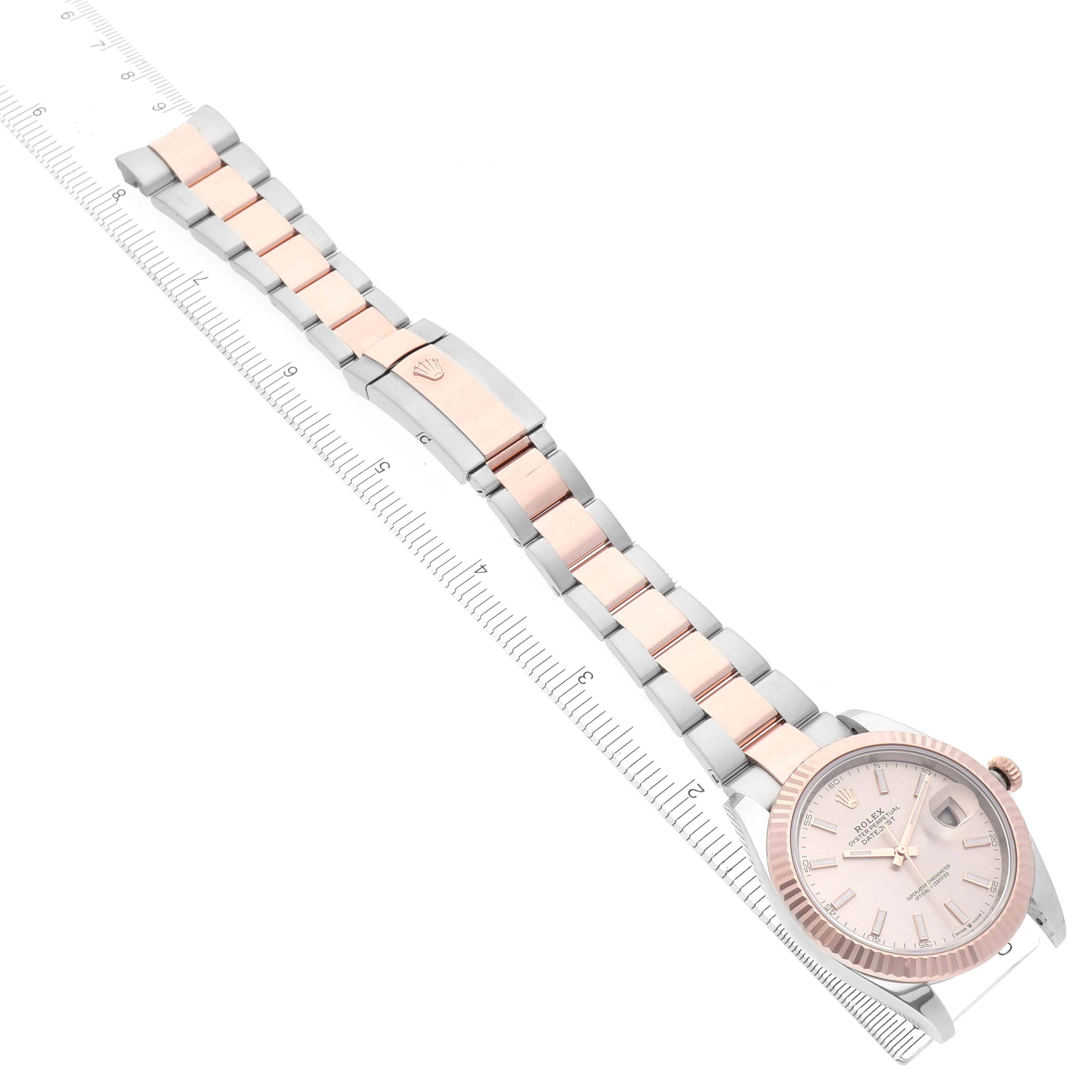 The Rolex Datejust 41 126331 Men's Steel and Gold (two tone) Pink Dial 126331 Men's Steel and Gold (two tone) Pink Dial is shown at an angle displaying the watch face, bracelet, and clasp alongside a ruler for scale.