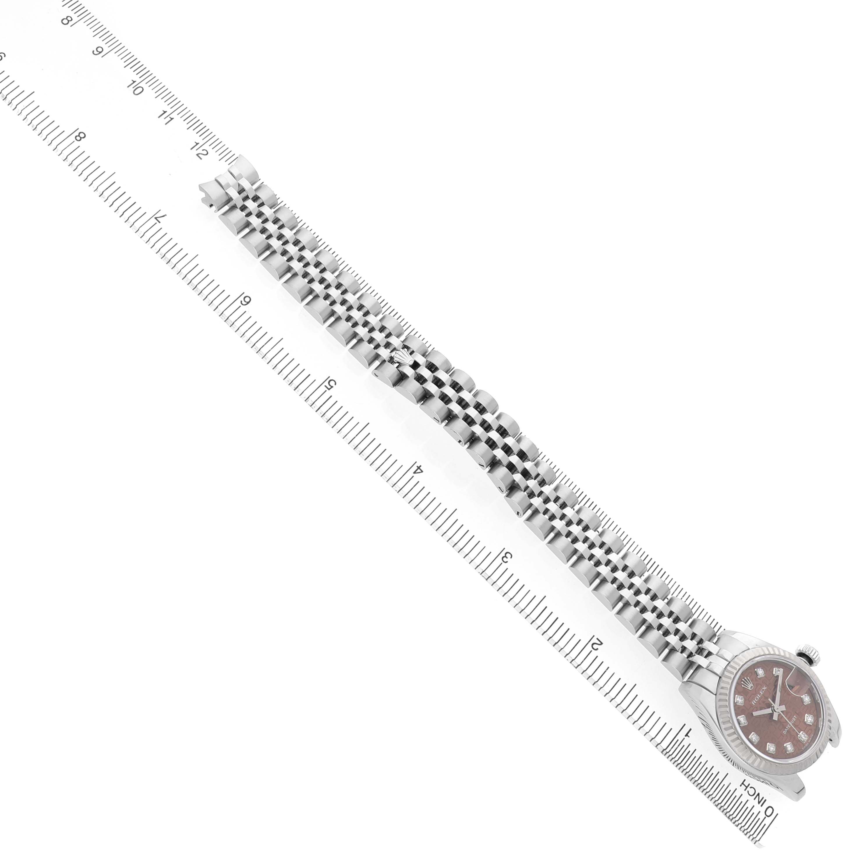 The image shows a Rolex Datejust 179174 Women's Stainless Steel Pink Dial watch from a top view, highlighting the face and metal bracelet alongside a ruler.