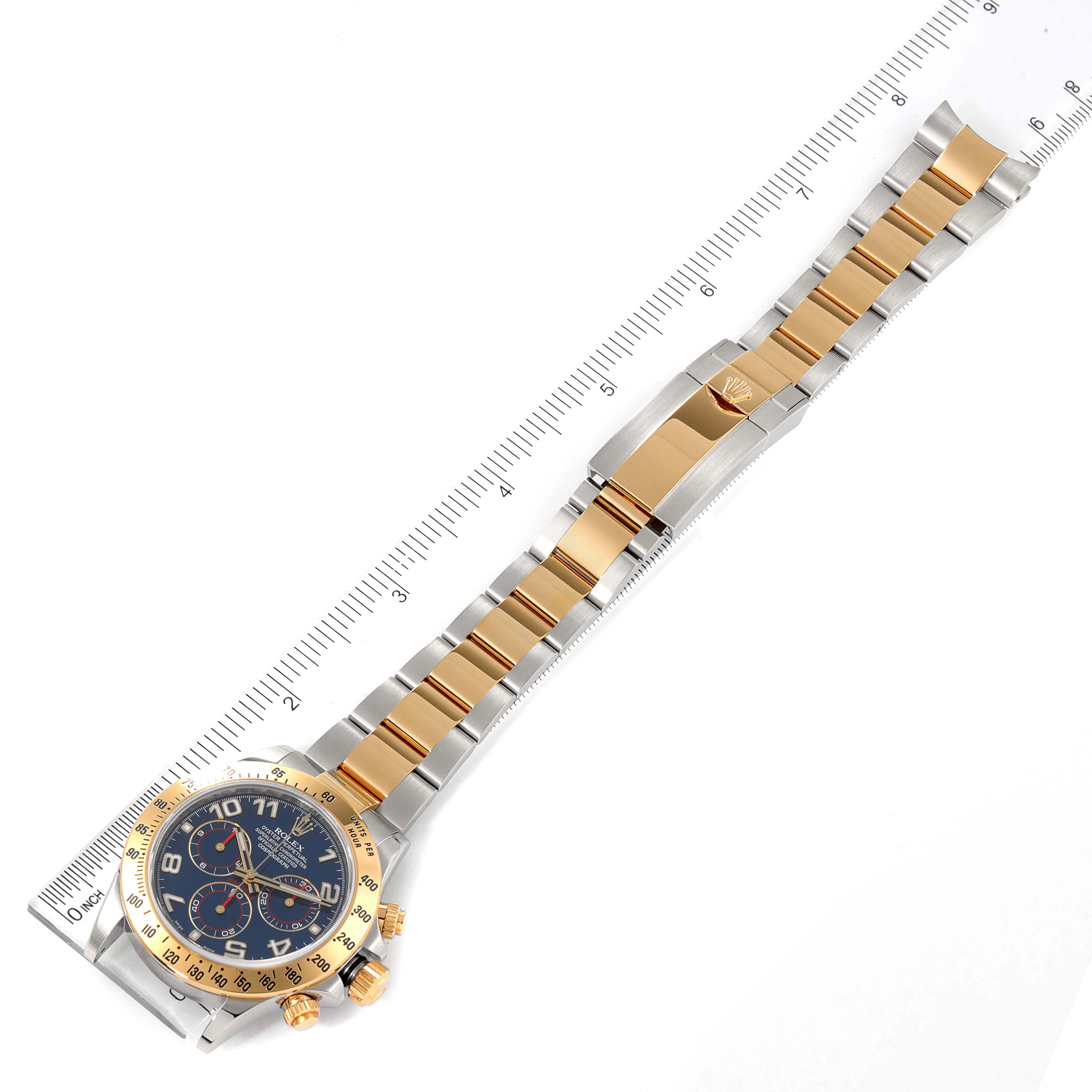 The image shows an overhead view of a Rolex Daytona 116523 Men's Steel and Gold (two tone) Blue Dial 116523 Men's Steel and Gold (two tone) Blue Dial watch, highlighting the face, bezel, and entire band with a ruler for scale.