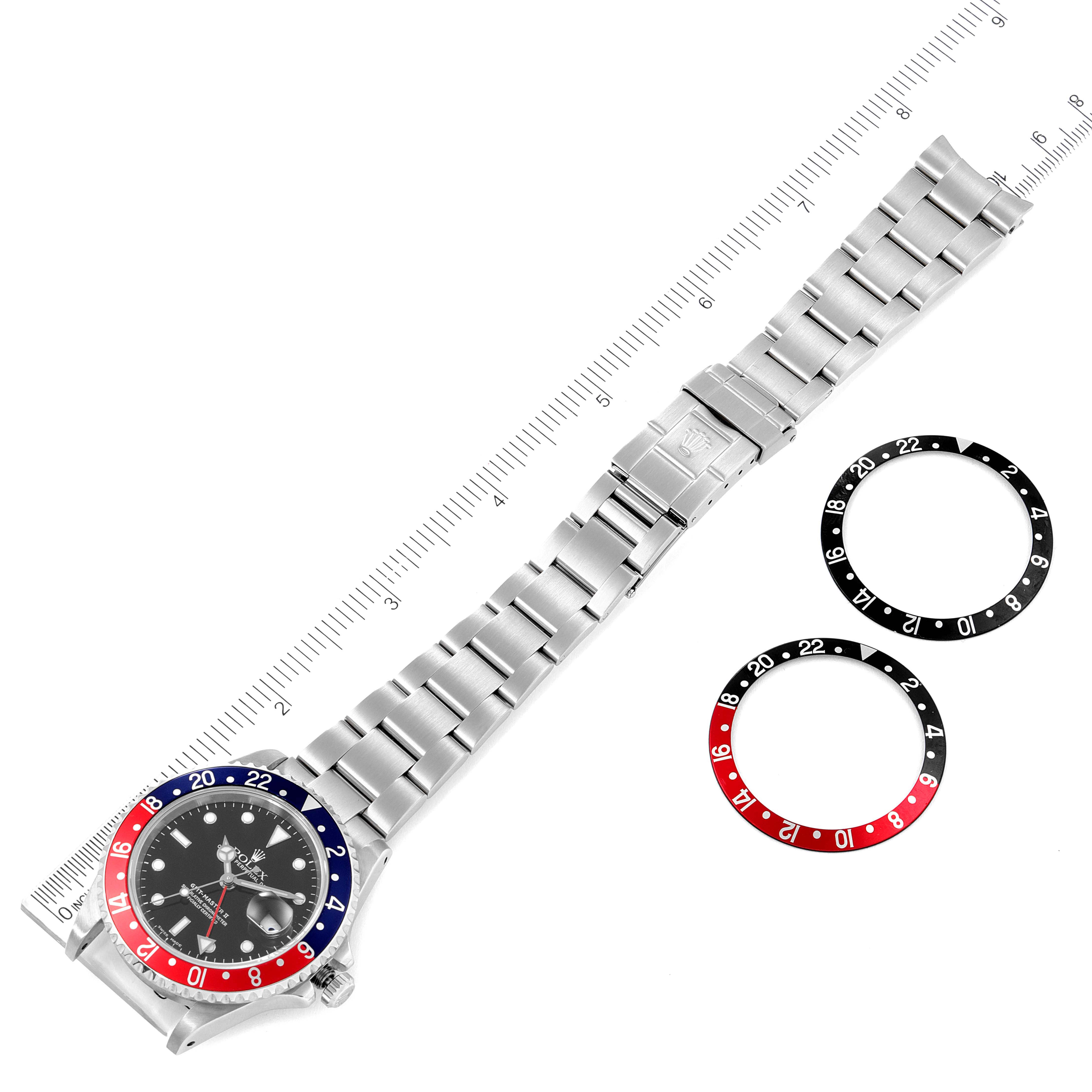 The image shows a Rolex GMT-Master 16710 Men
s Stainless Steel Black Dial 16710 Men
s Stainless Steel Black Dial watch with its bracelet and bezel inserts, viewed from above, alongside a ruler for scale.