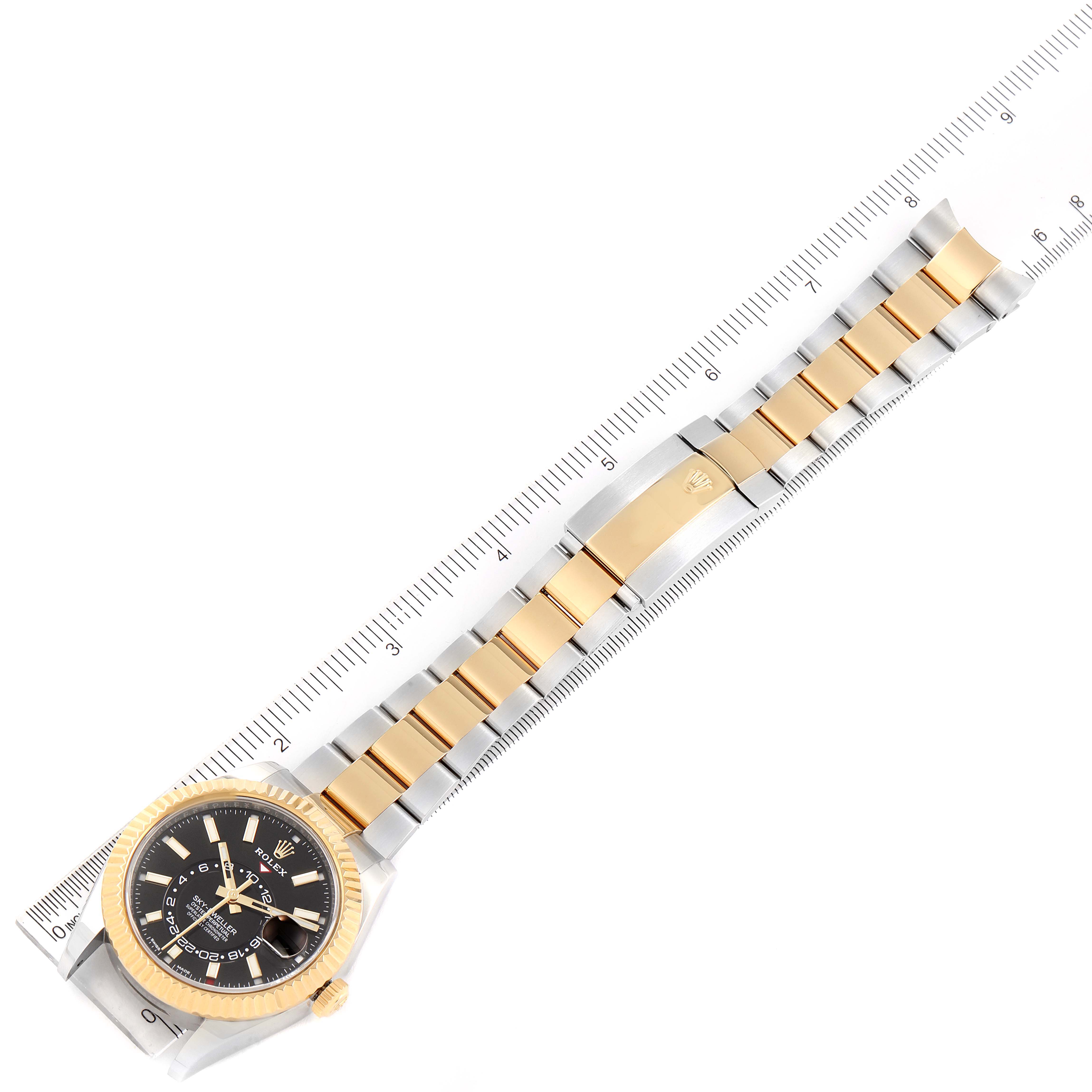 This image shows a top-down view of the Rolex Sky-Dweller 326933 Men's Steel and Gold (two tone) Black Dial 326933 Men's Steel and Gold (two tone) Black Dial watch, displaying its full bracelet and face next to a ruler for scale.