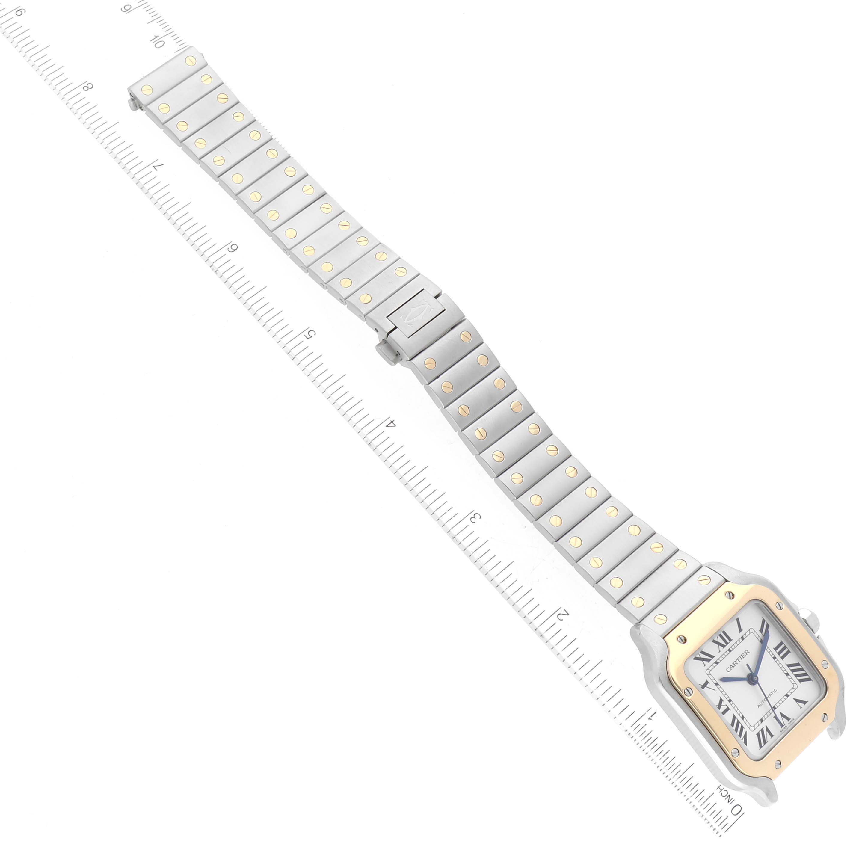 The Cartier Santos W2SA0007 Men's Steel and Gold (two tone) Silver Dial W2SA0007 Men's Steel and Gold (two tone) Silver Dial watch is shown from a top-down angle, displaying the face, band, and clasp with a ruler for scale.