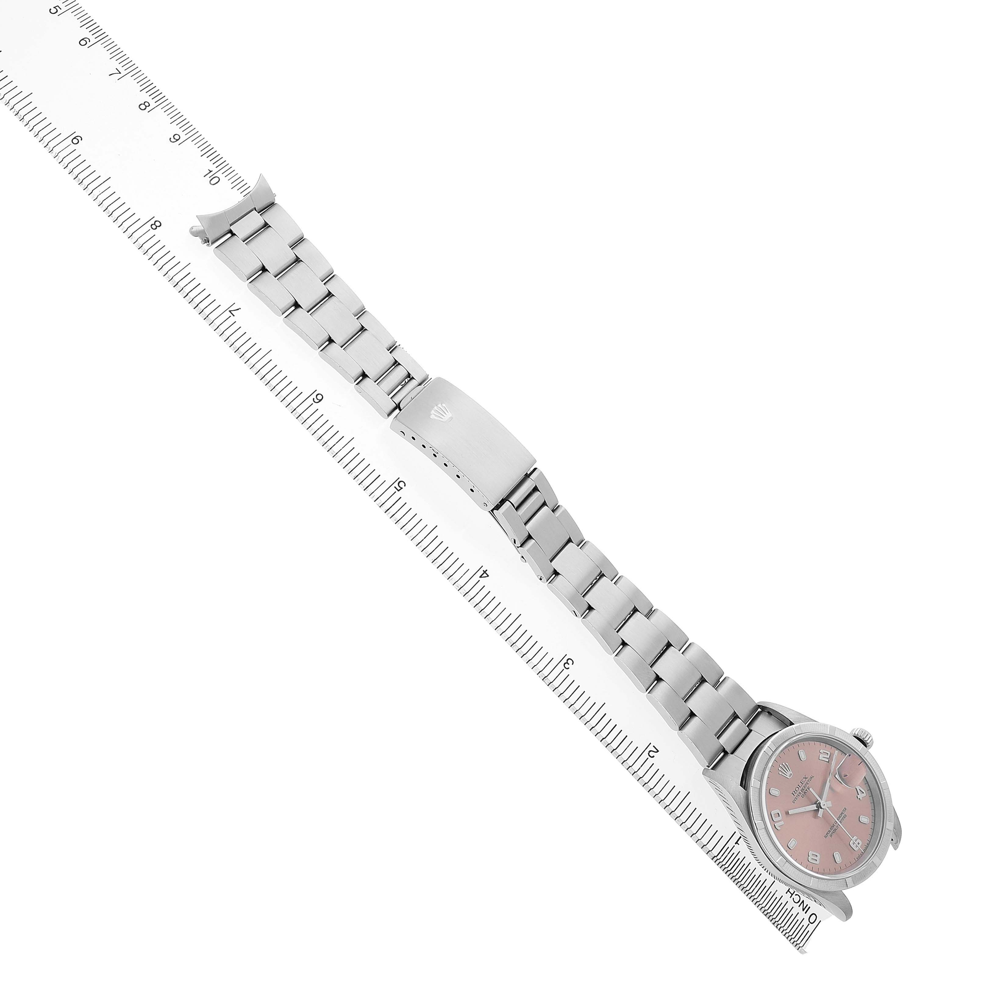 The Rolex Date 15210 Men's Stainless Steel Pink Dial watch is shown at a diagonal angle, displaying the face, bracelet, and clasp alongside a ruler.