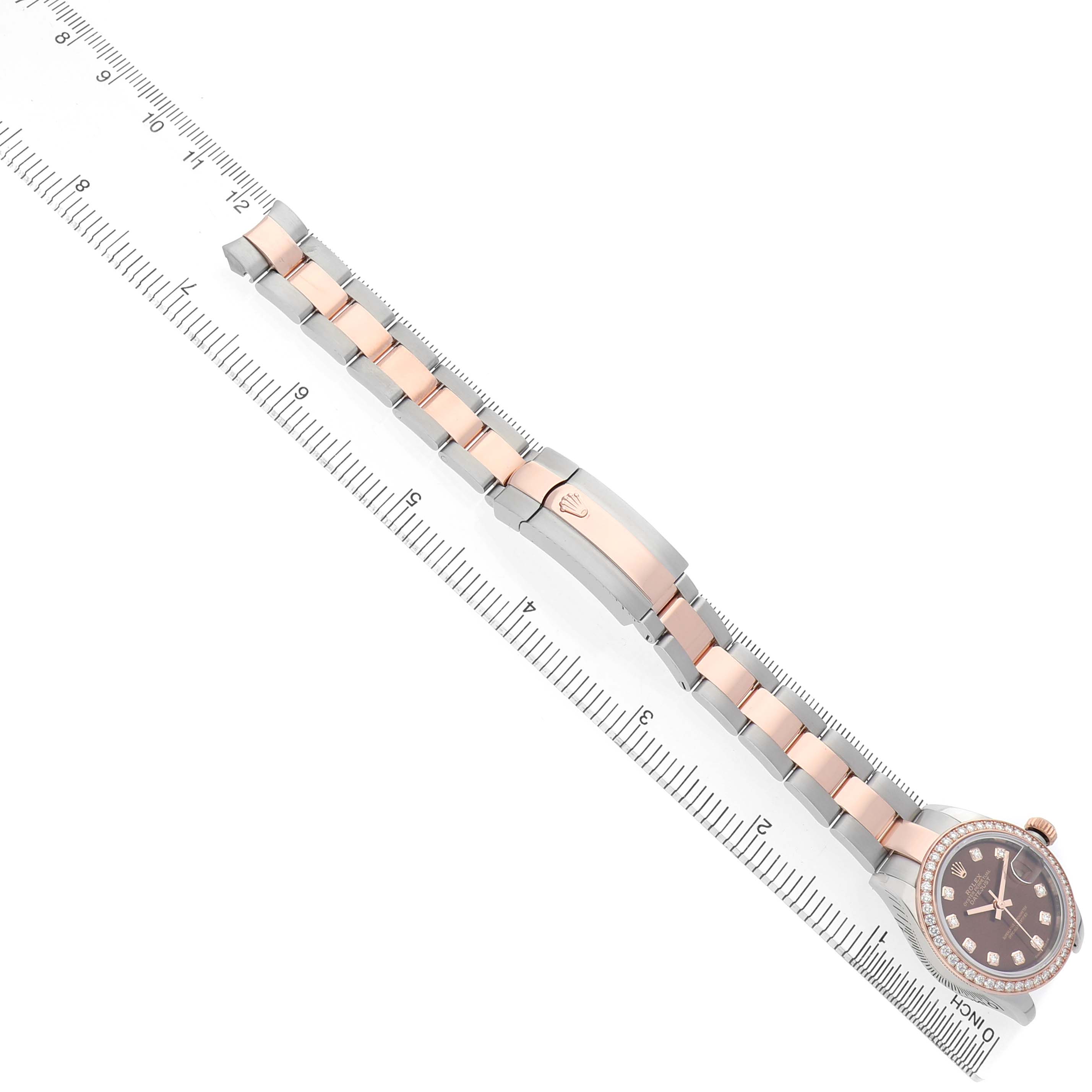 The Rolex Datejust 279381 Women's Steel and Gold (two tone) Brown Dial watch is shown from a top-down angle, highlighting the bracelet and clasp next to a ruler for scale.