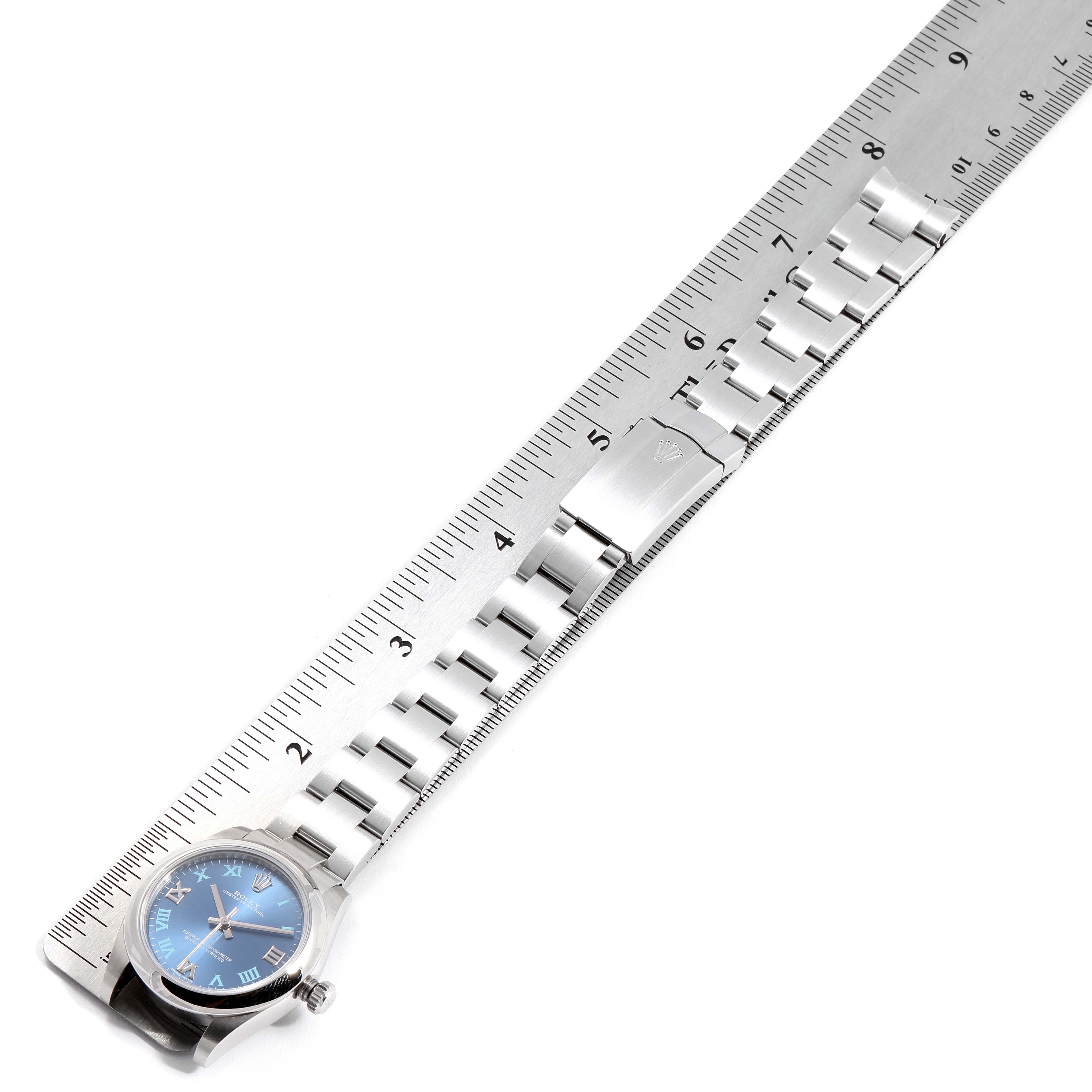 The image shows a top view of a Rolex Mid-Size 177200 Women
s Stainless Steel Blue Dial 177200 Women
s Stainless Steel Blue Dial model watch, highlighting its blue dial and stainless steel bracelet against a ruler.