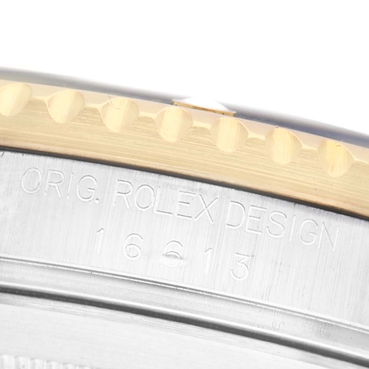 The image shows a close-up of the edge of a Rolex Submariner 16613 Men's Steel and Gold (two tone) Blue Dial's bezel with engraved text on the case.