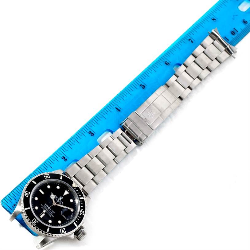 The image shows a Rolex Submariner 168000 Men
s Stainless Steel Black Dial 168000 Men
s Stainless Steel Black Dial watch laid flat next to a blue measurement ruler.