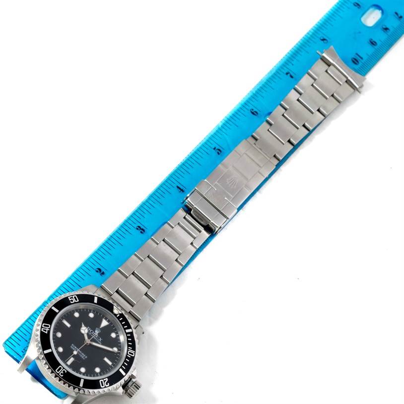 This image shows a top-down view of a Rolex Submariner 14060 Men
s Stainless Steel Black Dial 14060 Men
s Stainless Steel Black Dial watch with a metal bracelet and clasp, positioned next to a ruler.