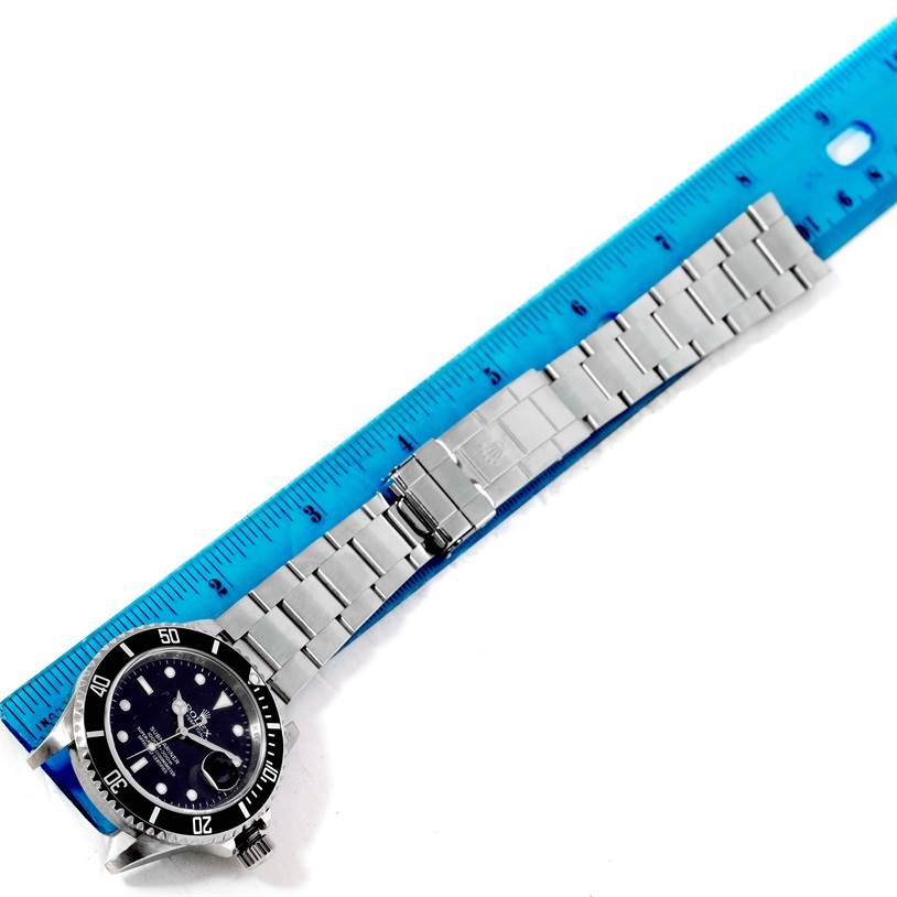 The image shows a top view of a Rolex Submariner 16610 Men
s Stainless Steel Black Dial 16610 Men
s Stainless Steel Black Dial watch with a blue ruler measuring its stainless steel bracelet.