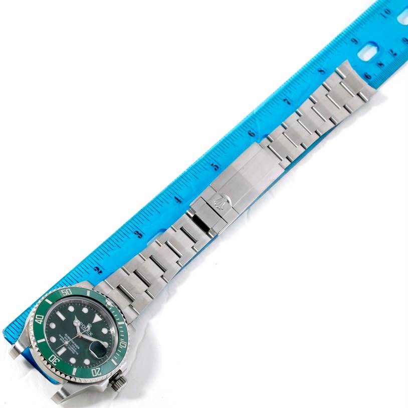 This image shows a top view of a Rolex Submariner 116610LV Men's Stainless Steel Green Dial 116610LV Men's Stainless Steel Green Dial watch with a teal bezel, stainless steel bracelet, and a blue ruler for scale.