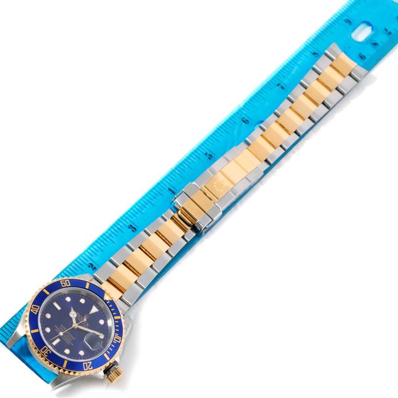 This image shows a top view of the Rolex Submariner 16613 Men
s Steel and Gold (two tone) Blue Dial 16613 Men
s Steel and Gold (two tone) Blue Dial watch with its bracelet aligned next to a blue ruler.