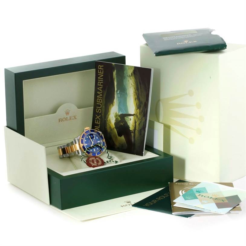 The image shows a Rolex Submariner 16613 Men
s Steel and Gold (two tone) Blue Dial 16613 Men
s Steel and Gold (two tone) Blue Dial watch with its original box, booklets, tags, and papers all laid out for display.