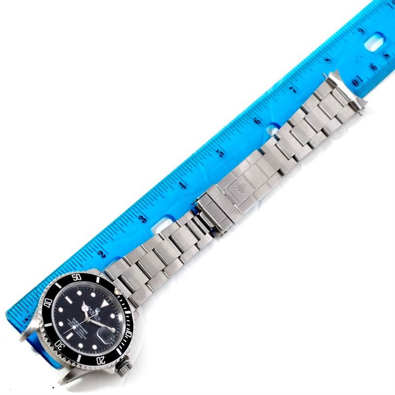 This image shows a Rolex Submariner 168000 Men
s Stainless Steel Black Dial 168000 Men
s Stainless Steel Black Dial watch laid flat next to a blue ruler, highlighting the length of the bracelet and clasp.