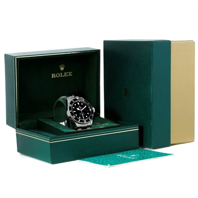 The image shows a Rolex Submariner 168000 Men
s Stainless Steel Black Dial 168000 Men
s Stainless Steel Black Dial watch placed inside its green branded box with additional packaging and documents visible.