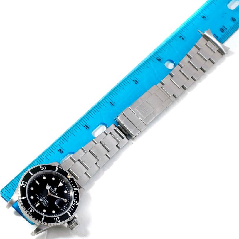 The image shows a Rolex Submariner 16610 Men
s Stainless Steel Black Dial 16610 Men
s Stainless Steel Black Dial watch, focusing on its face, bezel, and metal band, measured next to a scale ruler.