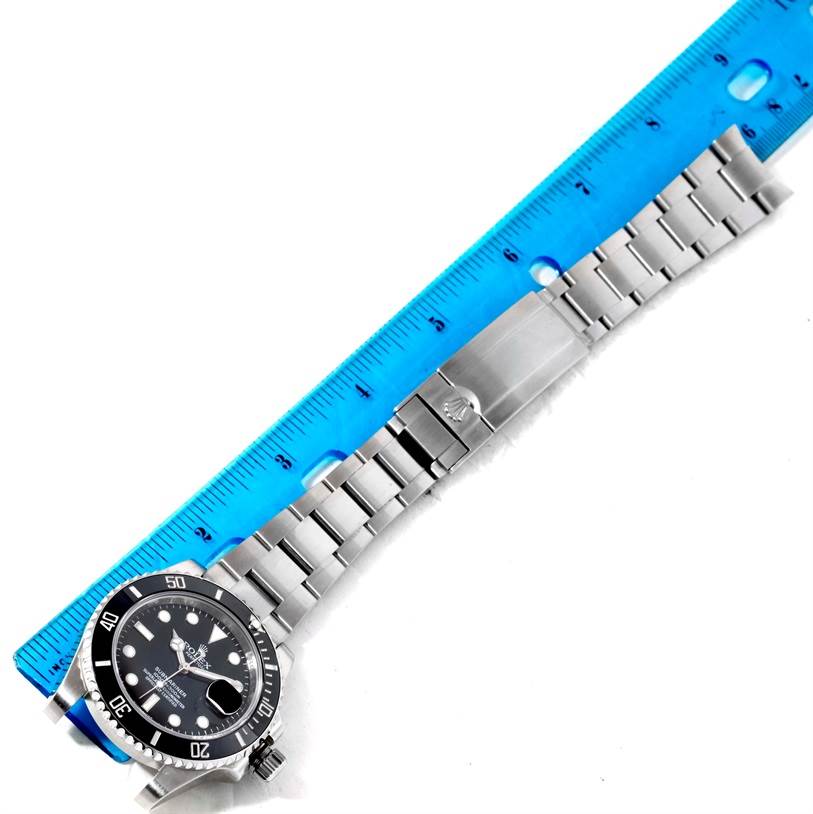 The image shows a top view of a Rolex Submariner 116610 Men
s Stainless Steel Black Dial 116610 Men
s Stainless Steel Black Dial watch with its metal bracelet placed alongside a blue ruler.