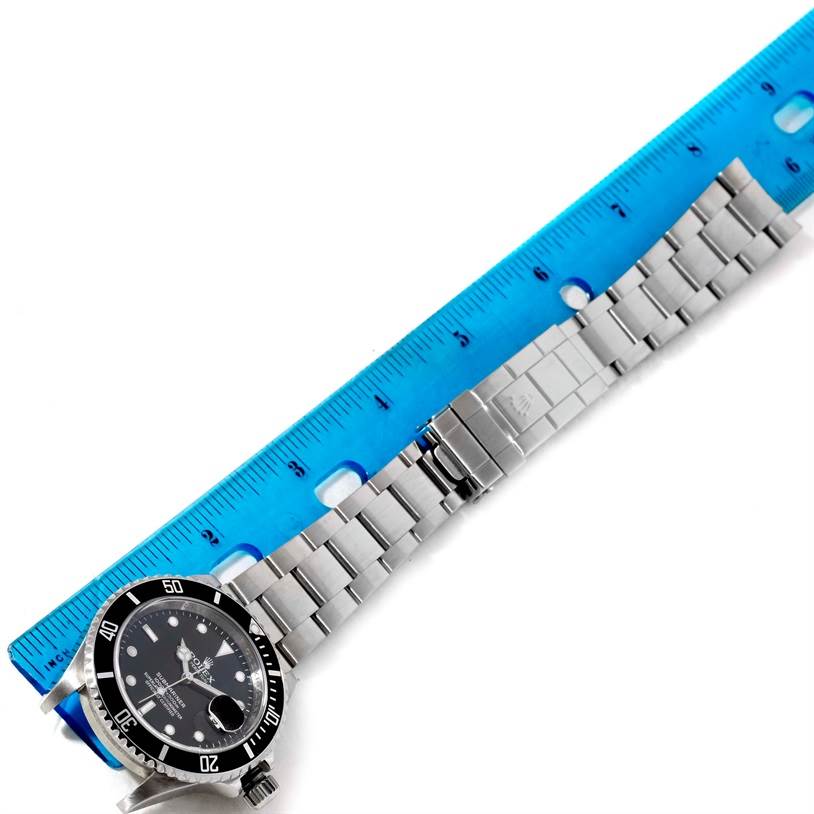 This image shows the Rolex Submariner 16610 Men
s Stainless Steel Black Dial 16610 Men
s Stainless Steel Black Dial watch laid flat next to a blue ruler, displaying the watch face and bracelet.