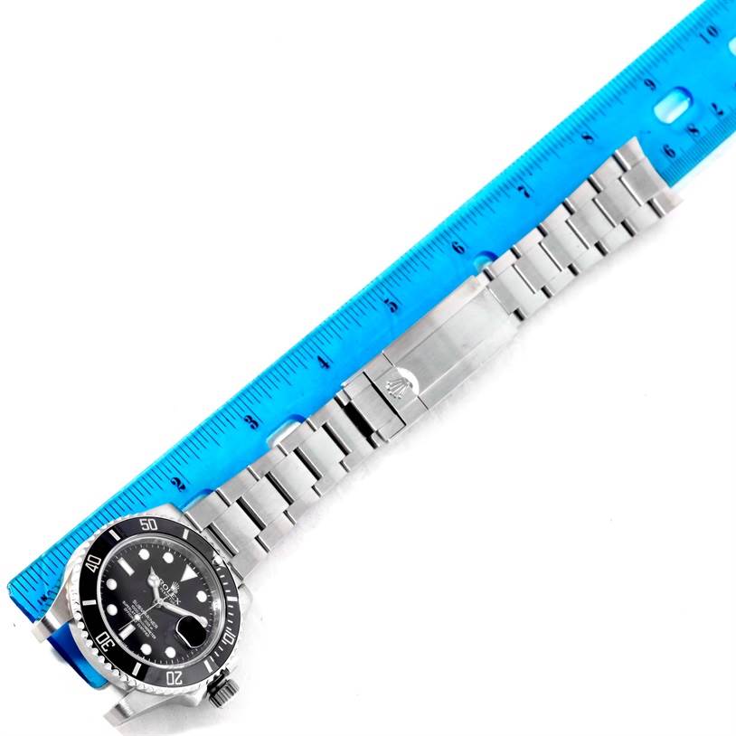 The image shows a Rolex Submariner 116610 Men
s Stainless Steel Black Dial 116610 Men
s Stainless Steel Black Dial watch laid flat with its stainless steel bracelet alongside a blue ruler for measurement.