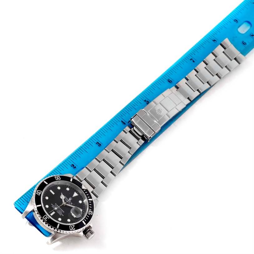 The Rolex Submariner 16610 Men
s Stainless Steel Black Dial 16610 Men
s Stainless Steel Black Dial watch is shown from an overhead angle, including its dial, bezel, and bracelet, alongside a ruler for scale.