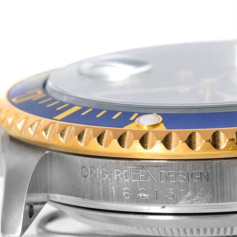 The image shows a close-up side angle of a Rolex Submariner 16613 Men's Steel and Gold (two tone) Blue Dial 16613 Men's Steel and Gold (two tone) Blue Dial, focusing on the bezel, crystal, and case with the engraving.