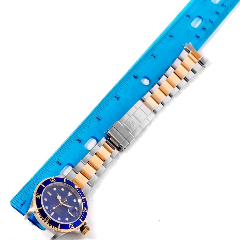 This image shows the front of a Rolex Submariner 16613 Men's Steel and Gold (two tone) Blue Dial 16613 Men's Steel and Gold (two tone) Blue Dial watch with its two-tone bracelet measuring against a blue ruler.