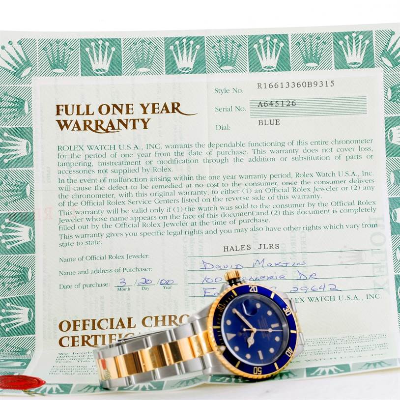 The image shows a Rolex Submariner 16613 Men's Steel and Gold (two tone) Blue Dial 16613 Men's Steel and Gold (two tone) Blue Dial watch placed on a full one-year warranty certificate, displaying its front and side.
