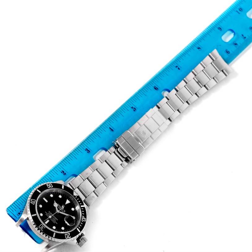 The Rolex Submariner 16610 Men
s Stainless Steel Black Dial 16610 Men
s Stainless Steel Black Dial watch is shown from a top-down angle alongside a blue ruler for scale.