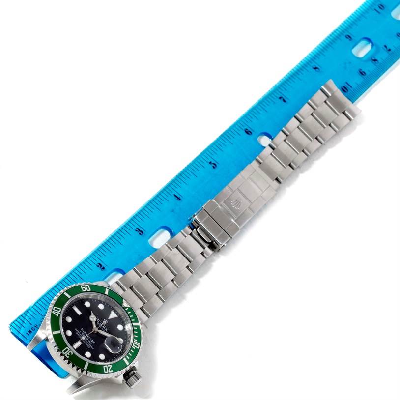 The image shows a Rolex Submariner 16610LV Men
s Stainless Steel Black Dial 16610LV Men
s Stainless Steel Black Dial watch with a green bezel and stainless steel bracelet, positioned next to a blue ruler.