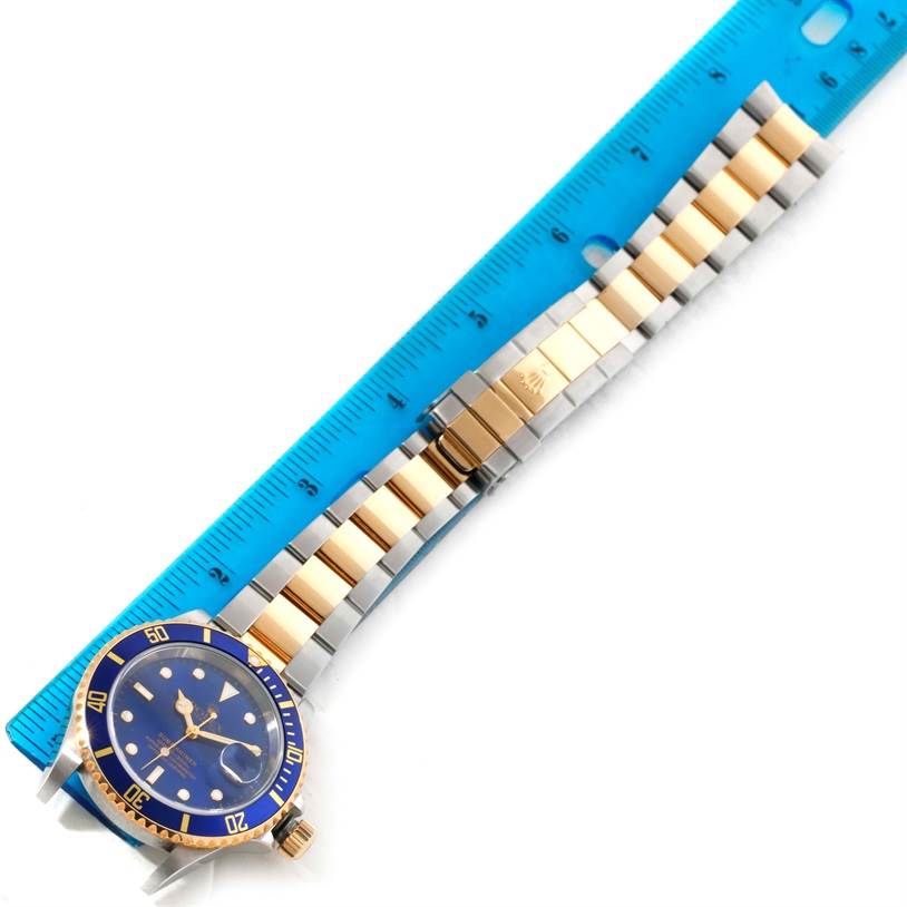 The Rolex Submariner 16613 Men's Steel and Gold (two tone) Blue Dial 16613 Men's Steel and Gold (two tone) Blue Dial watch is shown from a top view, displaying the dial, bezel, and bracelet alongside a ruler for scale.