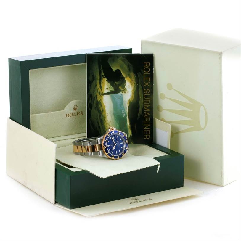 The Rolex Submariner 16613 Men's Steel and Gold (two tone) Blue Dial 16613 Men's Steel and Gold (two tone) Blue Dial watch is shown at an angle, displaying the dial, bracelet, and bezel, along with its box and documentation.