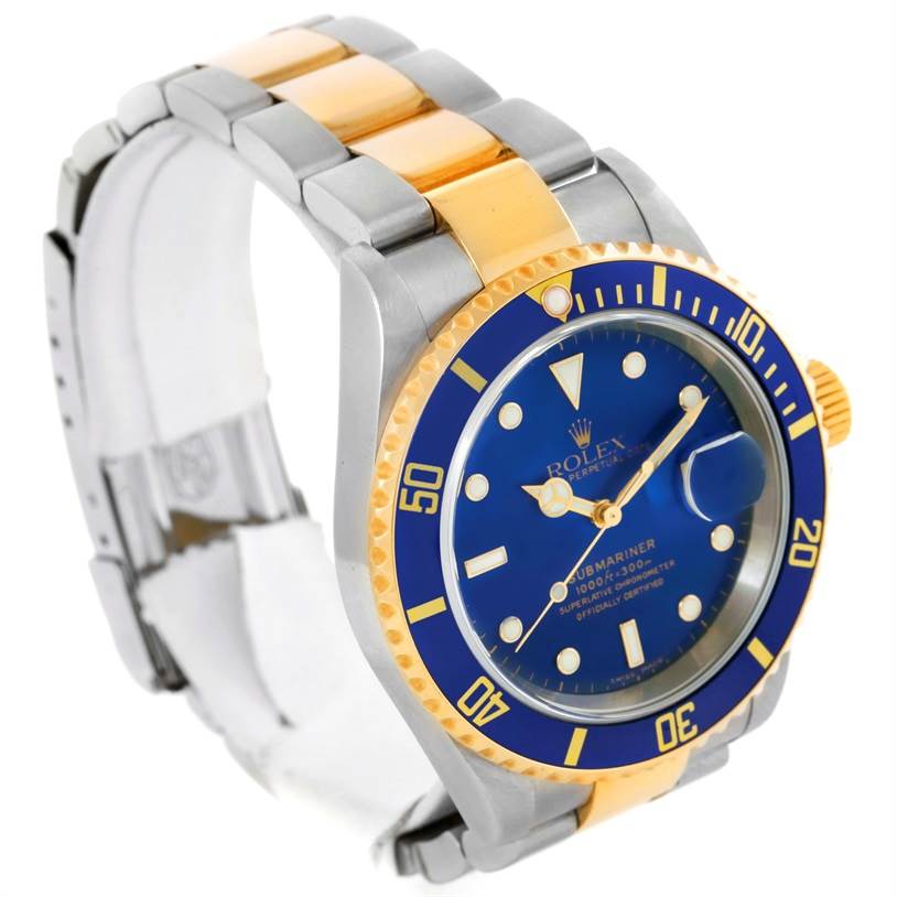 The image shows a Rolex Submariner 16613 Men's Steel and Gold (two tone) Blue Dial 16613 Men's Steel and Gold (two tone) Blue Dial watch from a 3/4 angle, highlighting its blue dial, yellow gold and steel bracelet, and bezel.